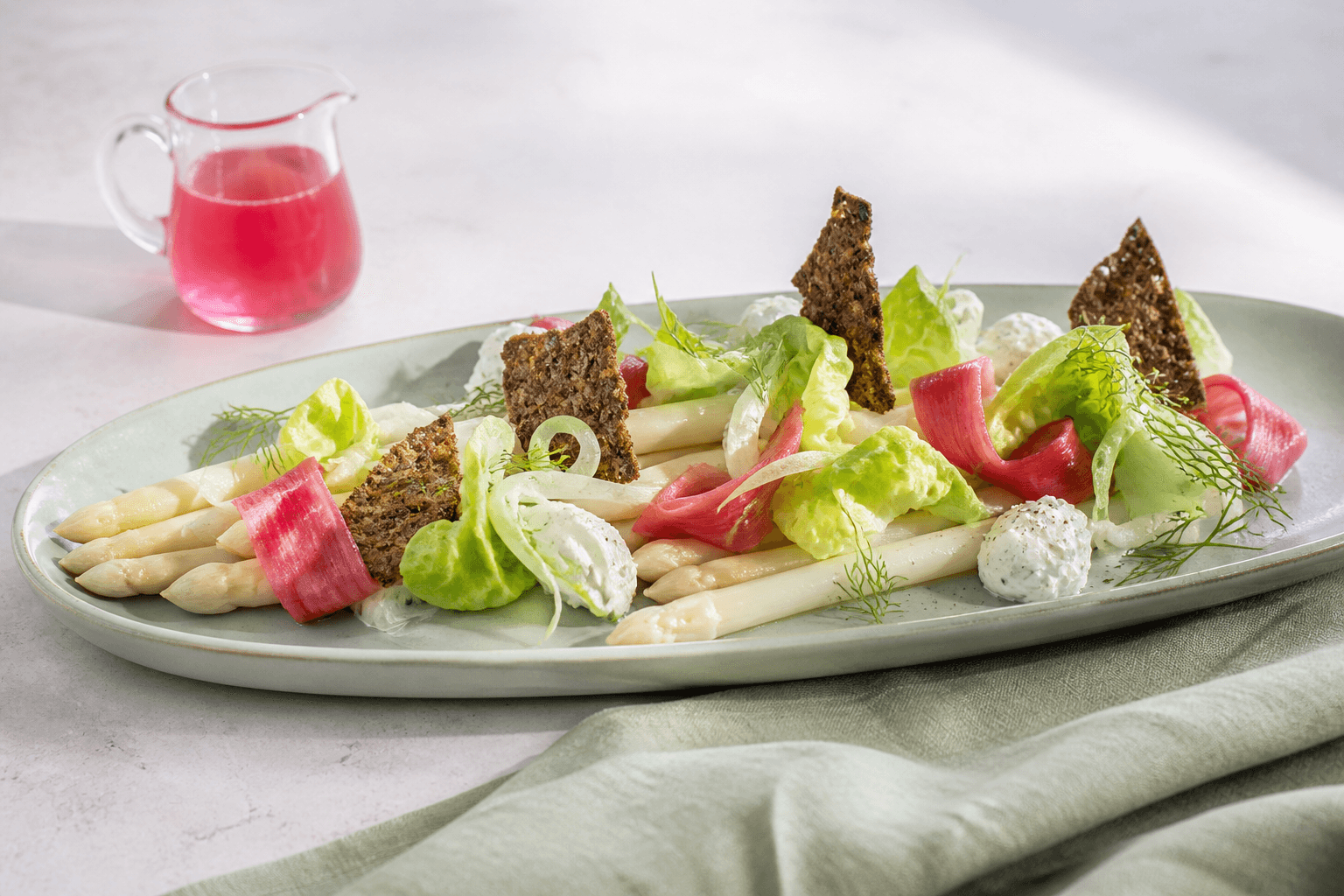 Forårssalat med hvide asparges, råsyltede rabarberbånd, fennikel, salat, kærnemælkscreme og sprøde rugflager på celadongrønt fad
