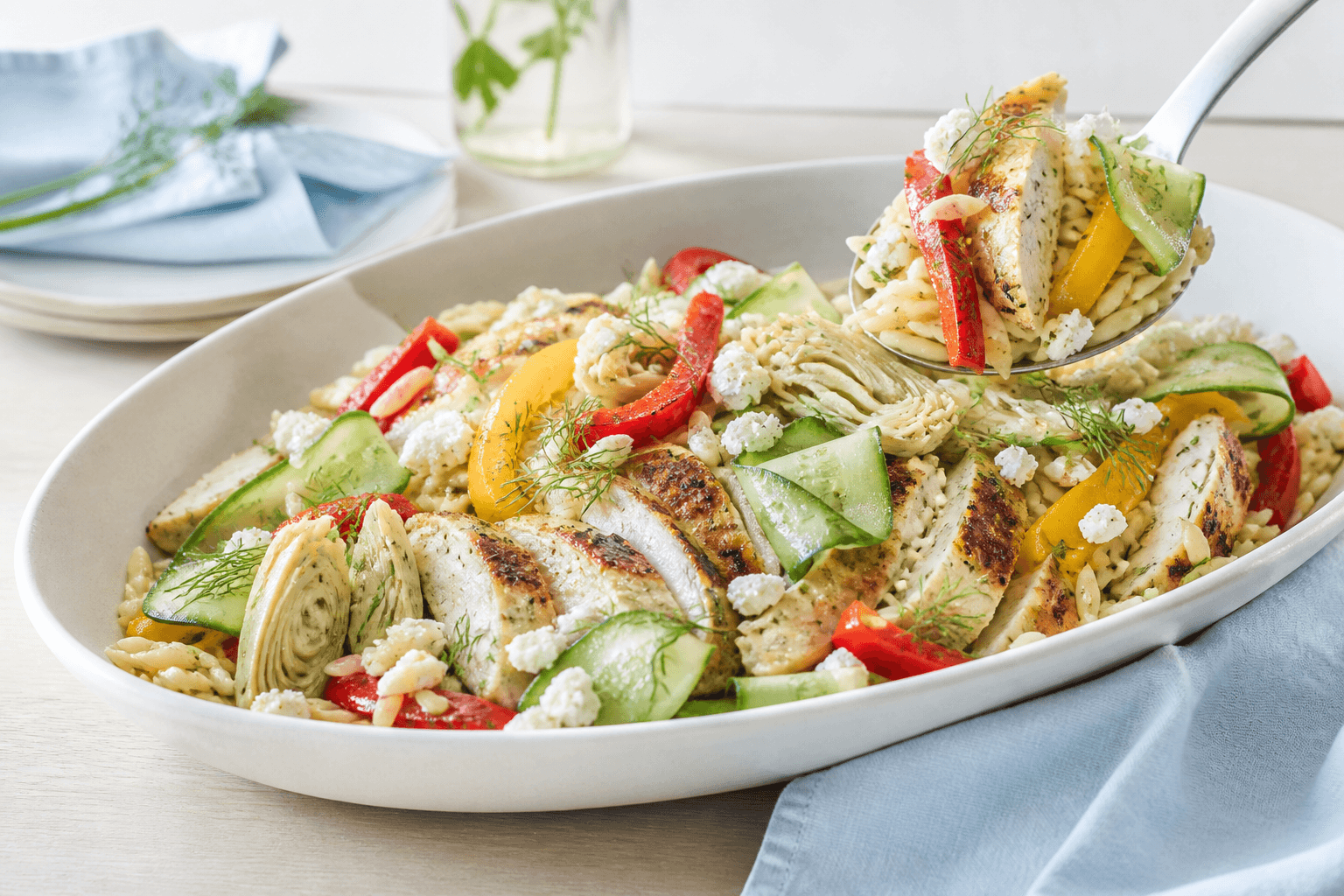 Orzopastasalat med citronkylling, grillede peberfrugter, artiskok, agurk, feta og dild i langt elfenbensfad