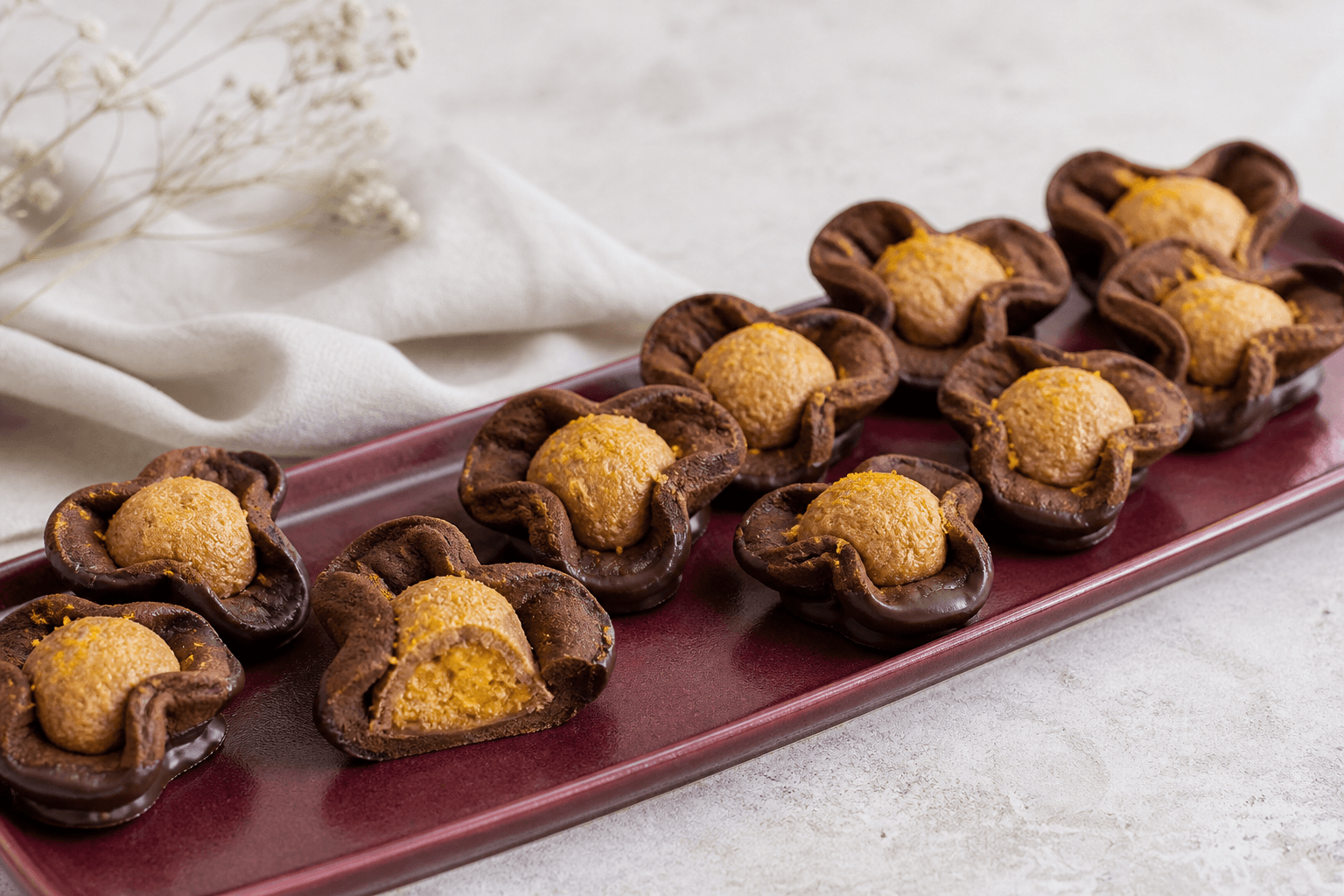 Små Napoleonshatte med mørk kakaomørdej, appelsinmarcipan, pistacie og mørk chokoladekant på bordeaux fad