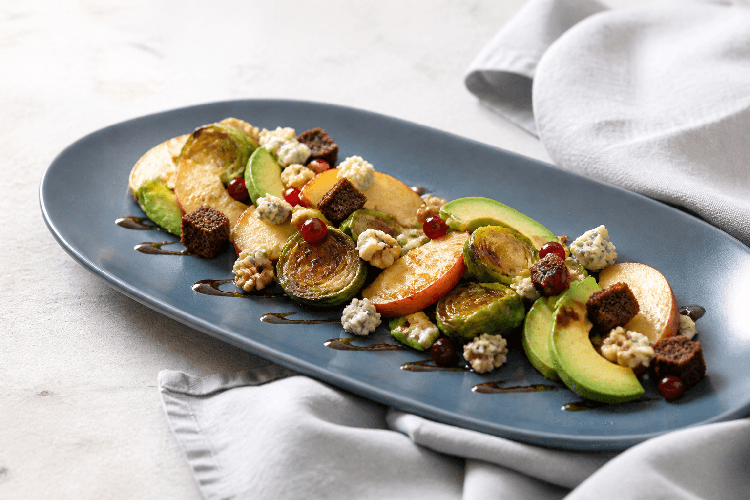 Lun rosenkålssalat med stegte røde æbler, avocado, blåskimmelost, rugcroutoner, valnødder og ribs på langt blågråt fad