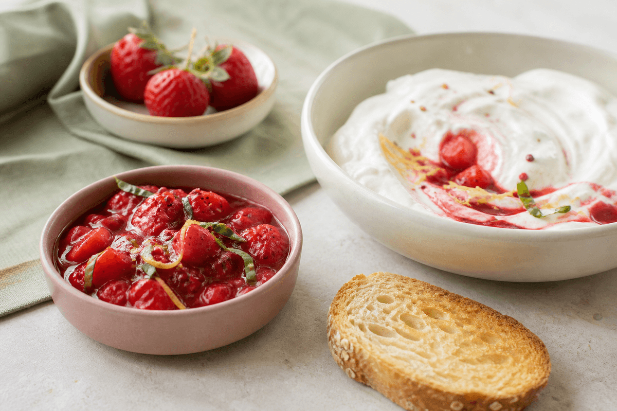 Blank jordbærkompot med hele bærstykker, basilikum, citron og pink peber i støvet rosa skål ved skyr og ristet brød