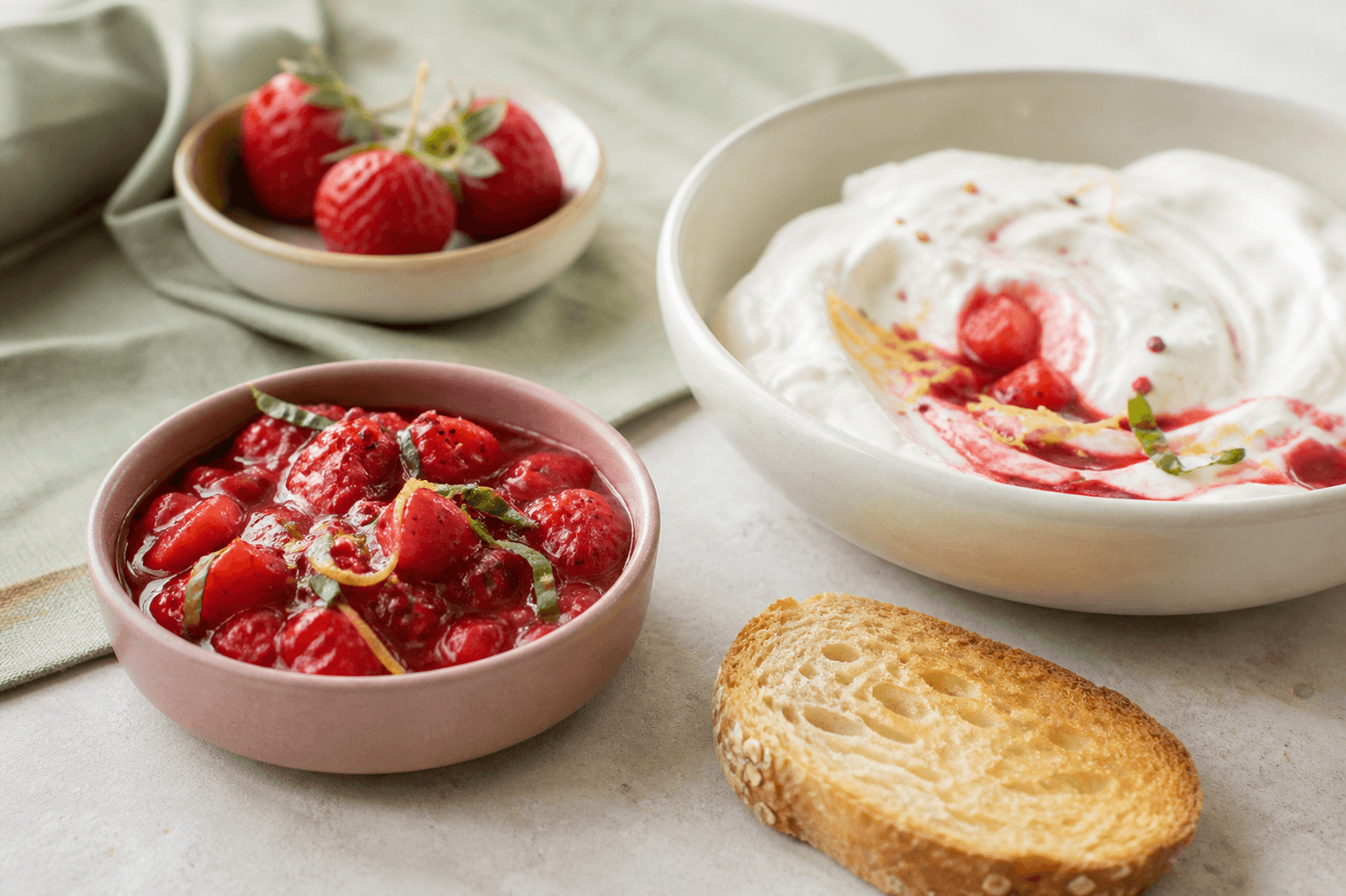 Blank jordbærkompot med hele bærstykker, basilikum, citron og pink peber i støvet rosa skål ved skyr og ristet brød