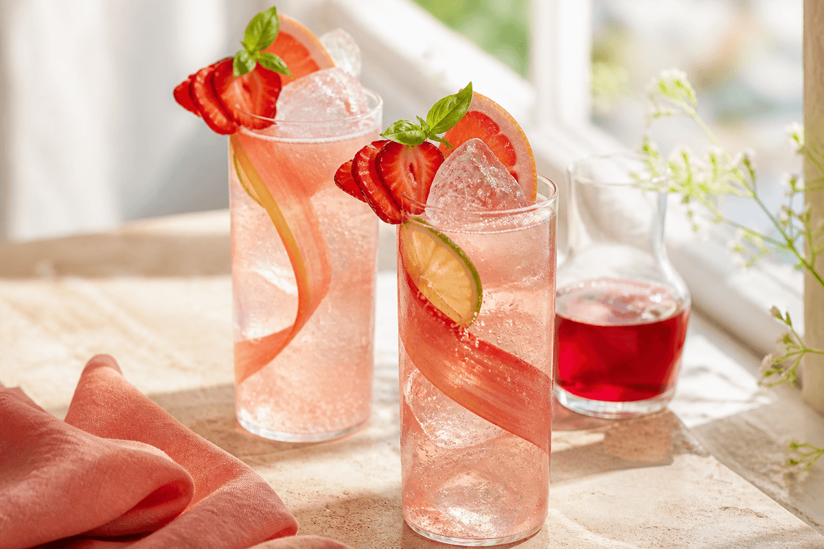 To høje jordbær-rabarber gin spritz med isspyd, rabarberbånd, jordbær, grapefrugt og basilikum