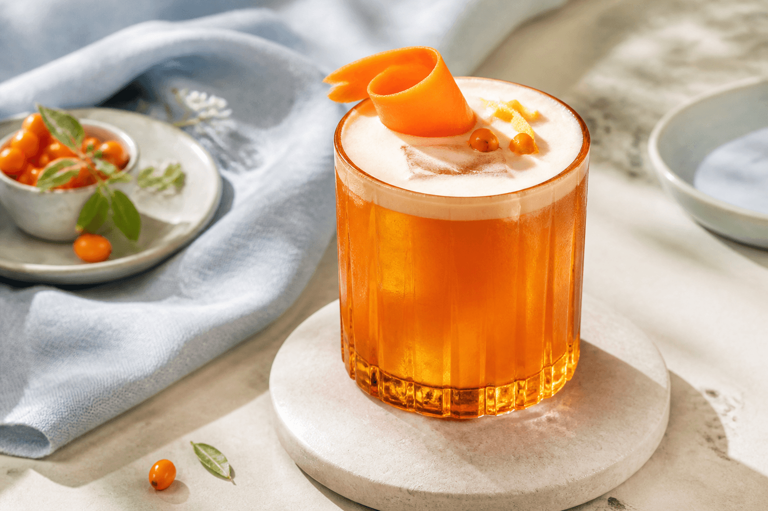 Orange havtorn-gulerod-gin sour med silkeblødt skum, gulerodsbånd, havtorn og citronskal i facetteret ravfarvet glas