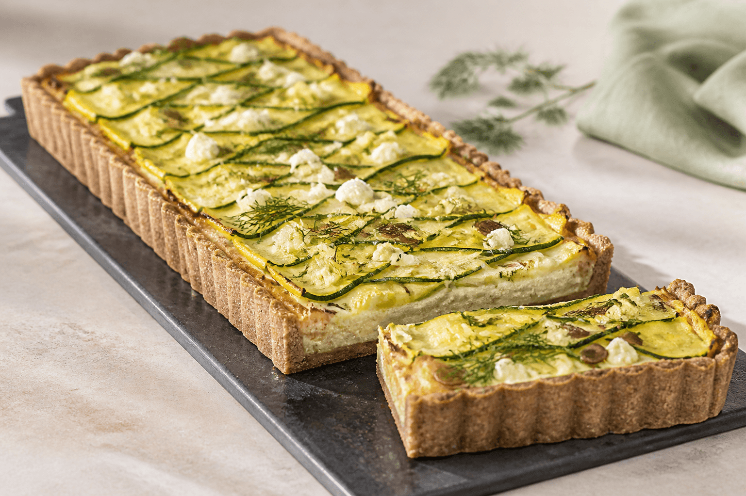Lang rektangulær squashtærte med rug-boghvedebund, citronricotta, grønne og gule squashbånd, porre, feta, dild og græskarkerner samt ét udtaget stykke