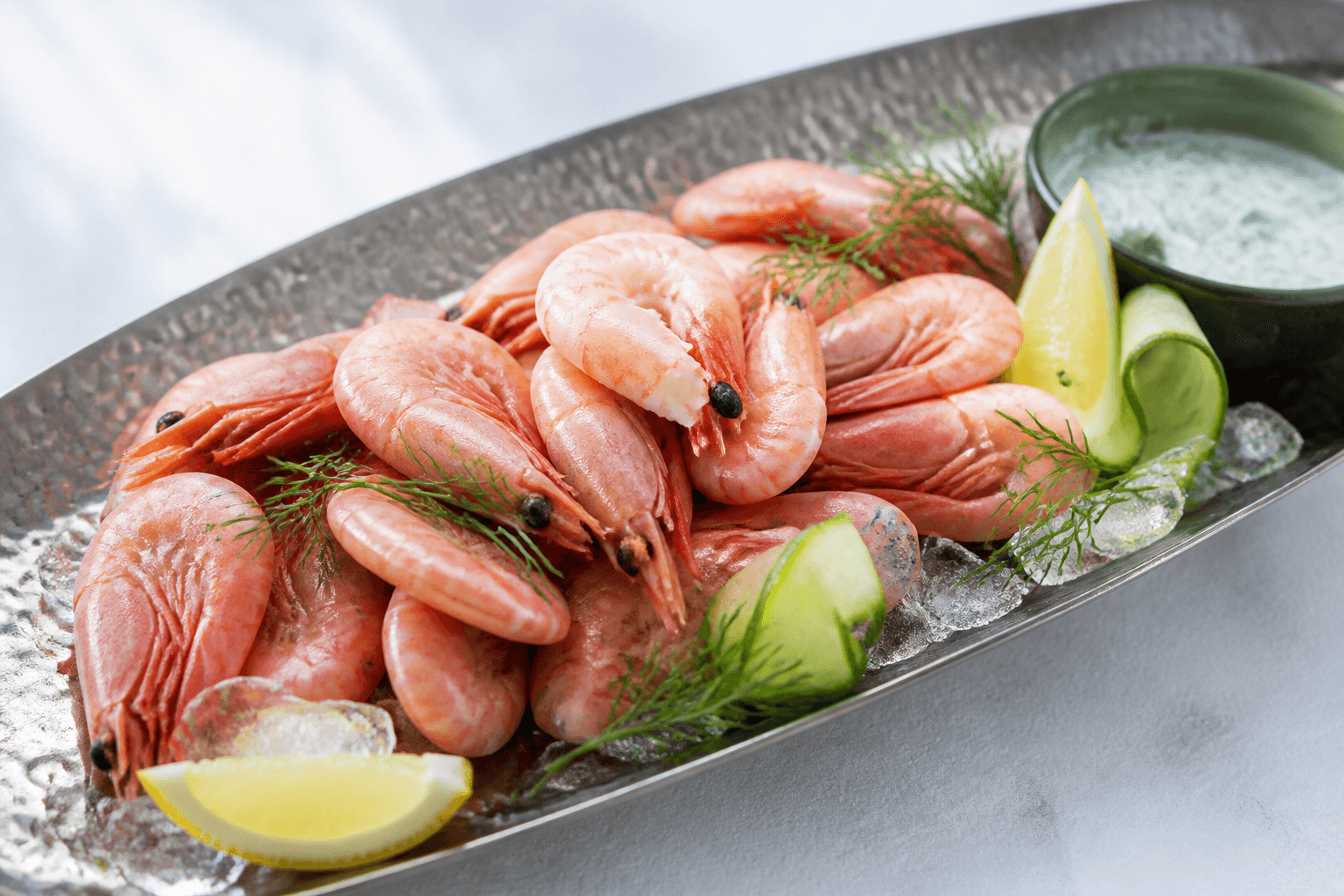 Pil selv-rejer på knust is i langt hamret metalfad med citron, dild, agurk og en skål grøn dilddressing