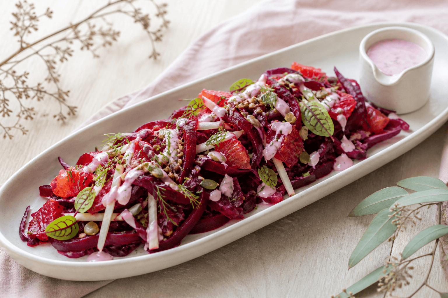 Langt lyst fad med rødbedeslaw, rødkål, pære, blodappelsin, lyserød peberrodsdressing, dild og ristede kerner