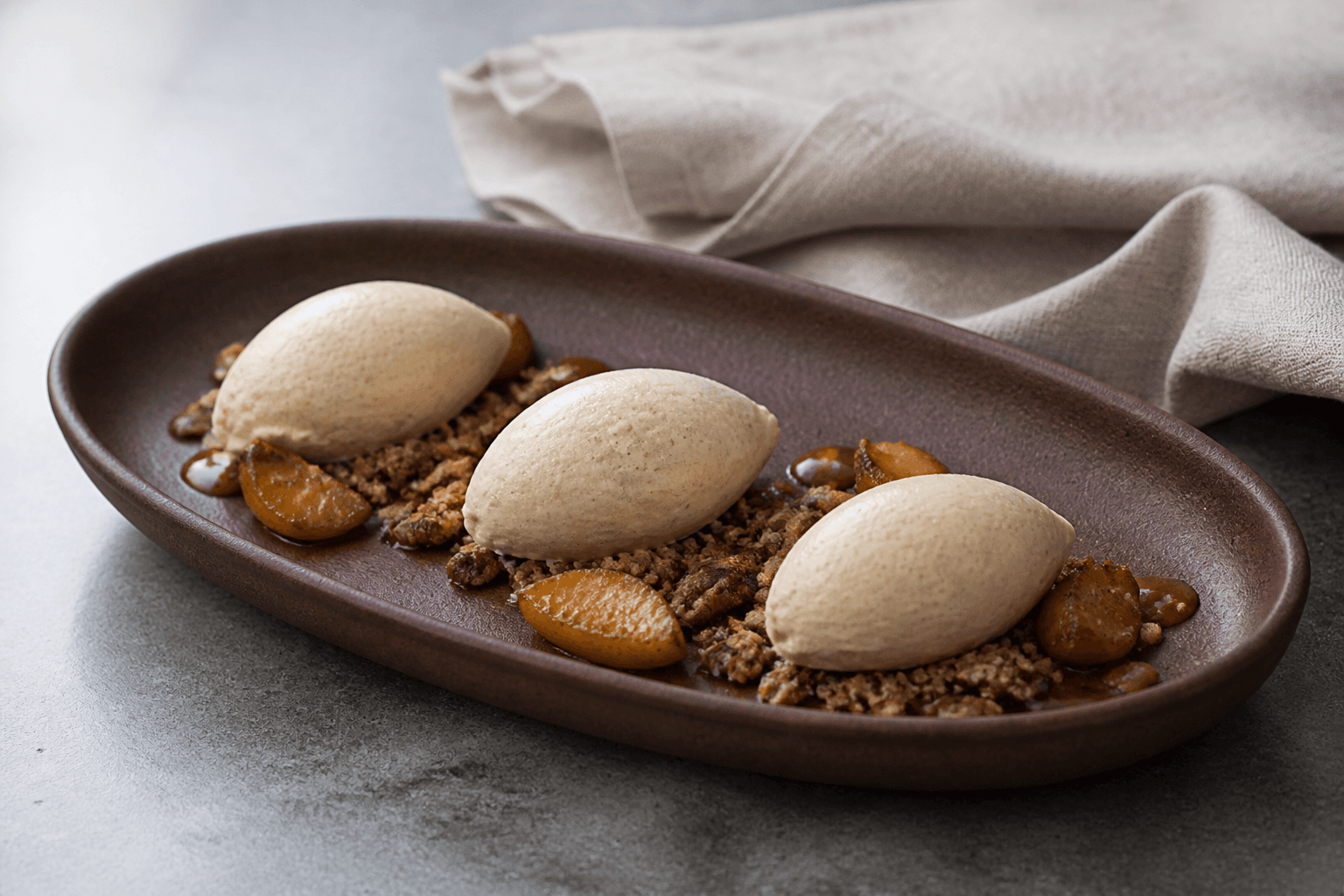 Tre ovale queneller lys kanelis med bagte æbler, havre-pecancrumble og blank ciderkaramel i langt mørkebrunt fad