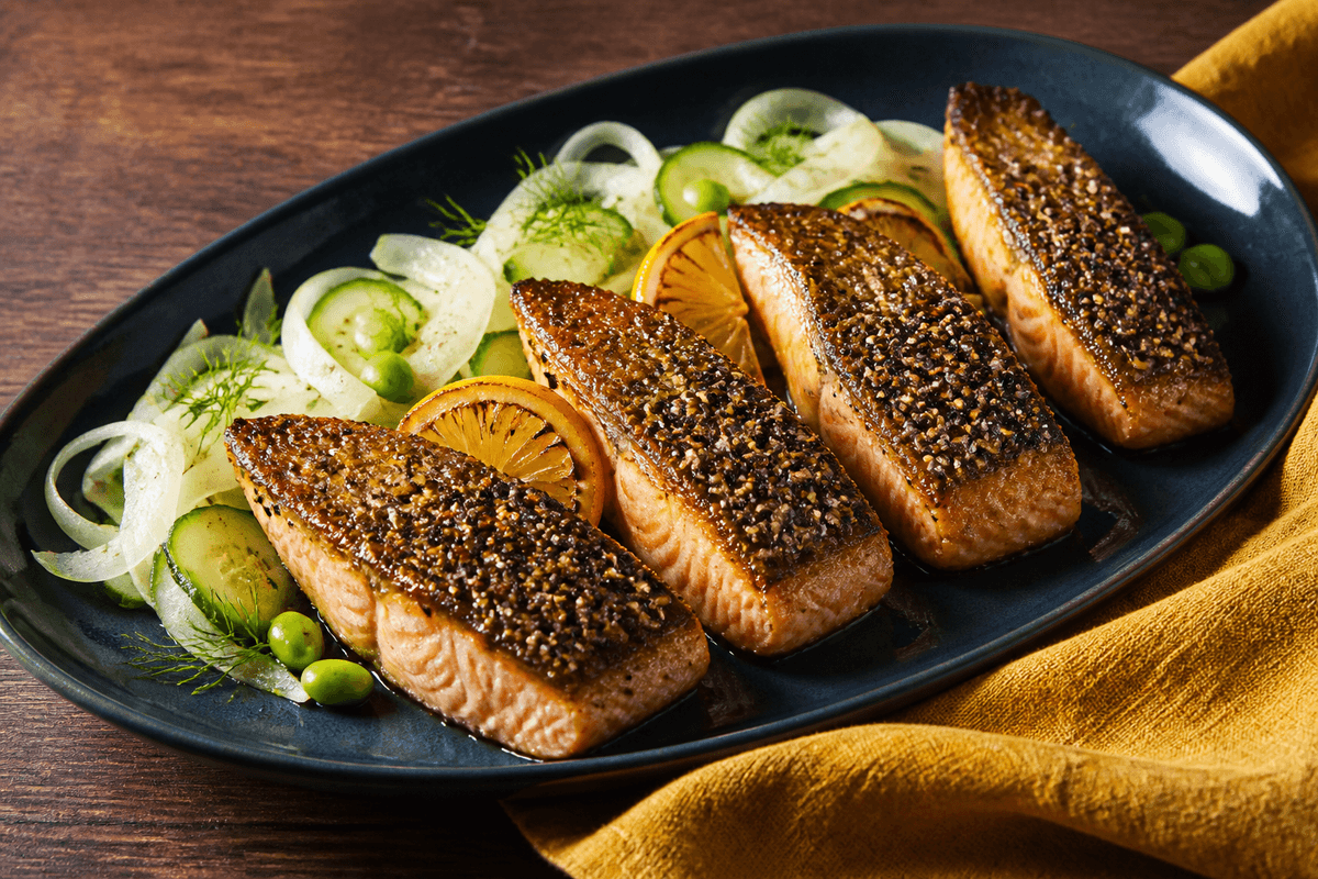 Fire gennemtilberedte laksefileter med sort-hvid sesamskorpe og citron-misoglace på indigo fad med fennikel, agurk, edamame og dild
