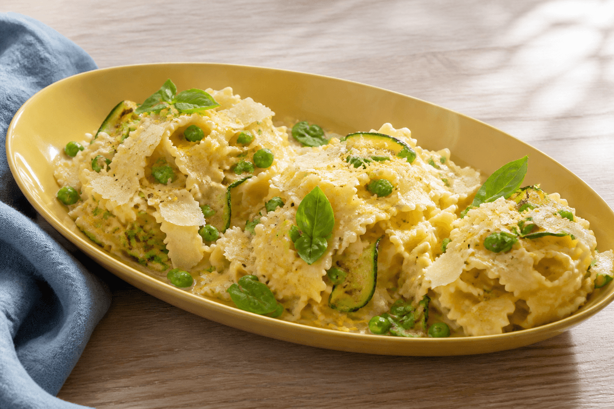Langt gult fad med brede pastabånd i cremet citron-parmesanemulsion, grønne ærter, grillede courgetter, basilikum og parmesanflager