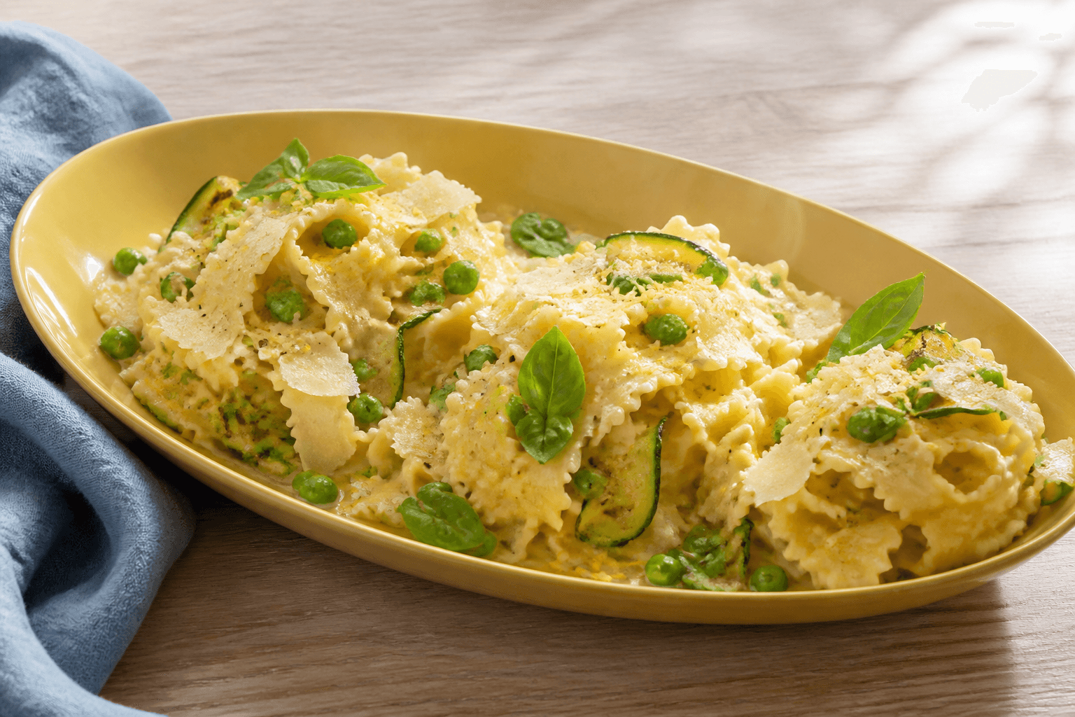 Langt gult fad med brede pastabånd i cremet citron-parmesanemulsion, grønne ærter, grillede courgetter, basilikum og parmesanflager