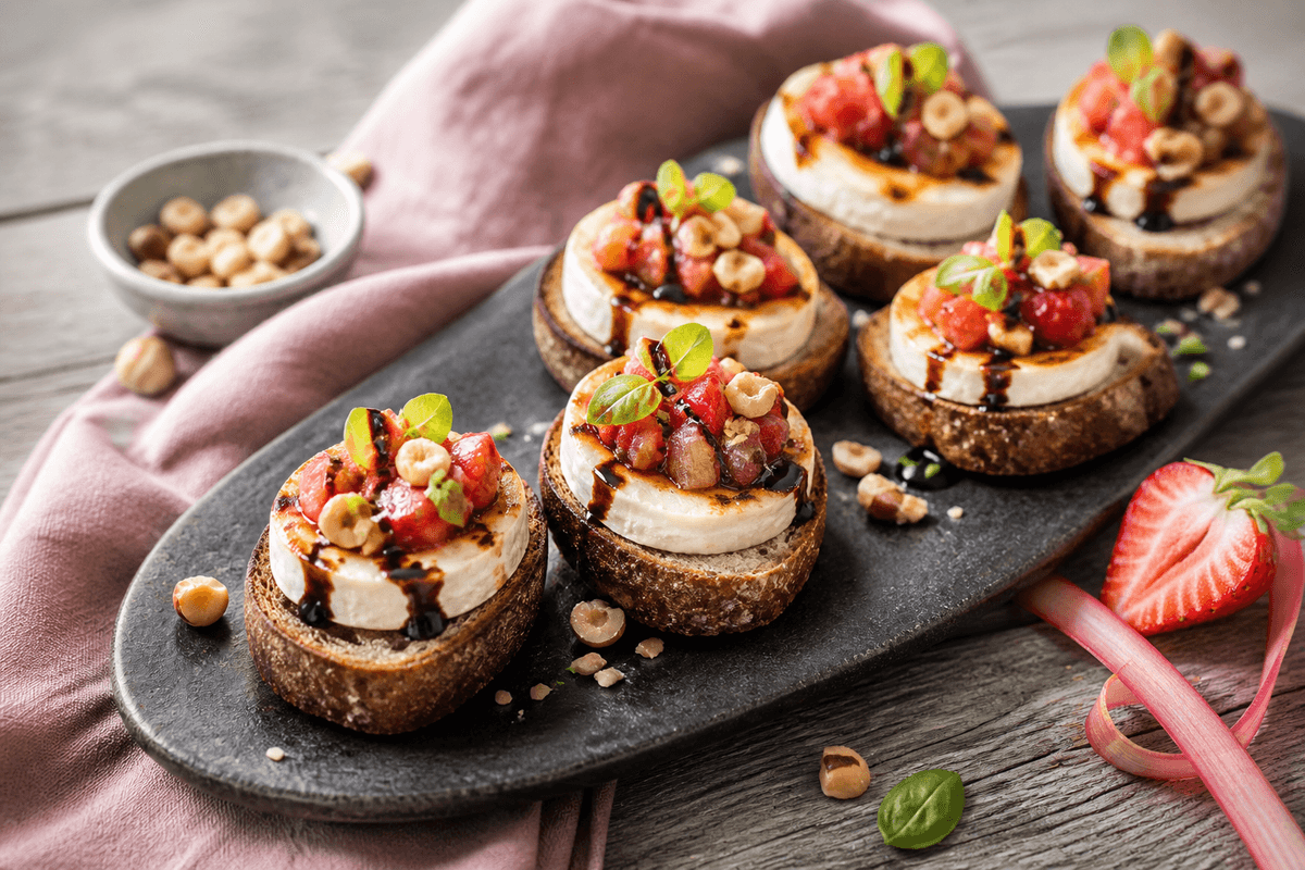 Seks mørke crostini med lun grillet gedeost, jordbær-rabarberrelish, balsamico, hasselnødder og basilikum på sort fad