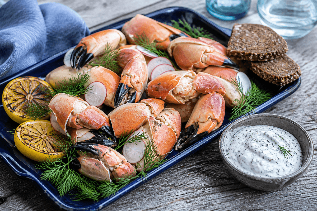 Kogte orange krabbeklør med dild, radiser, grillede citroner, rugbrød og dild-sennepsskyr på mørkeblåt fad