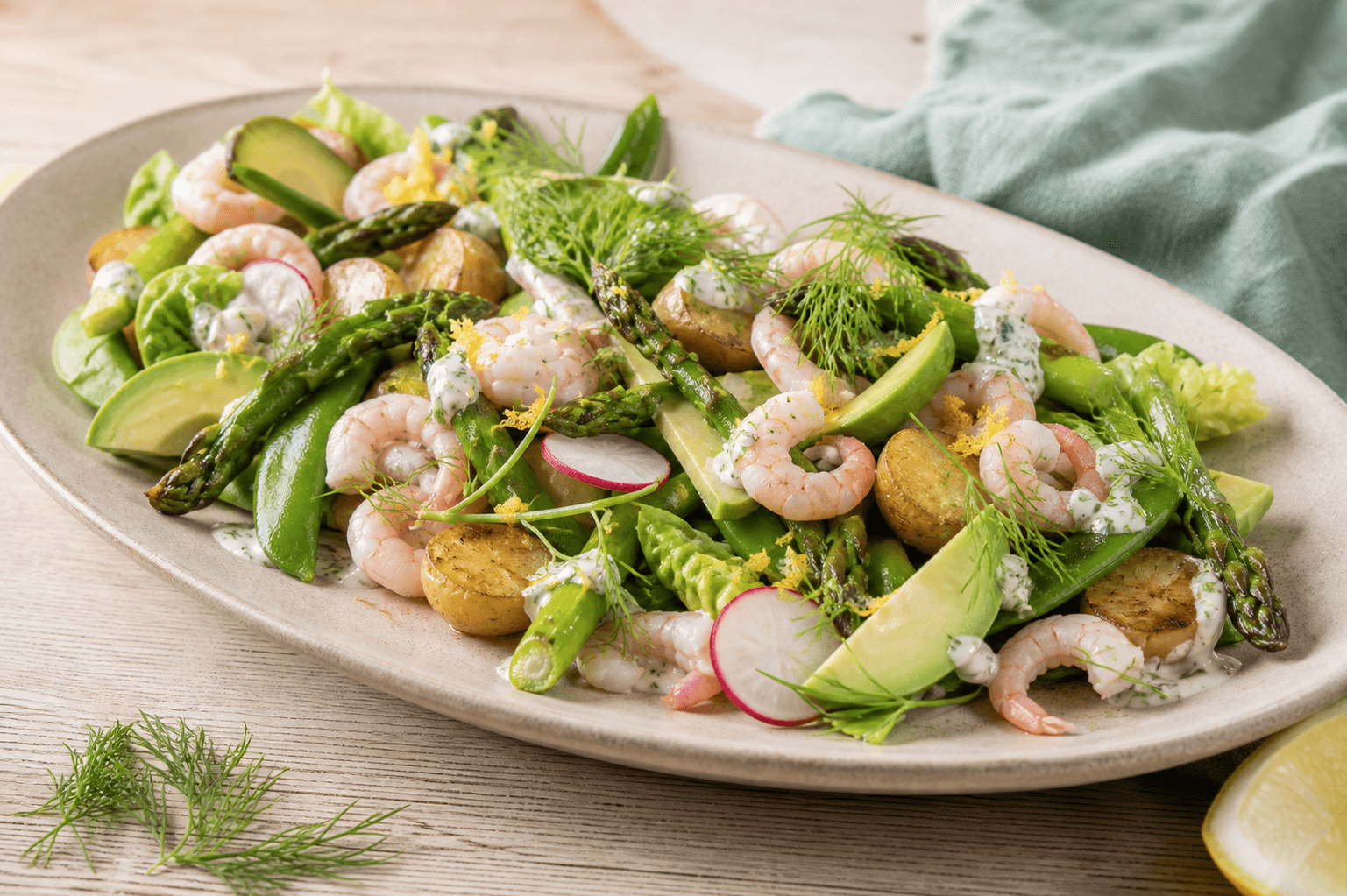 Rejesalat med rosa rejer, ristede nye kartofler, grønne asparges, avocado, sukkerærter, radiser og dildskyr på sandfarvet fad