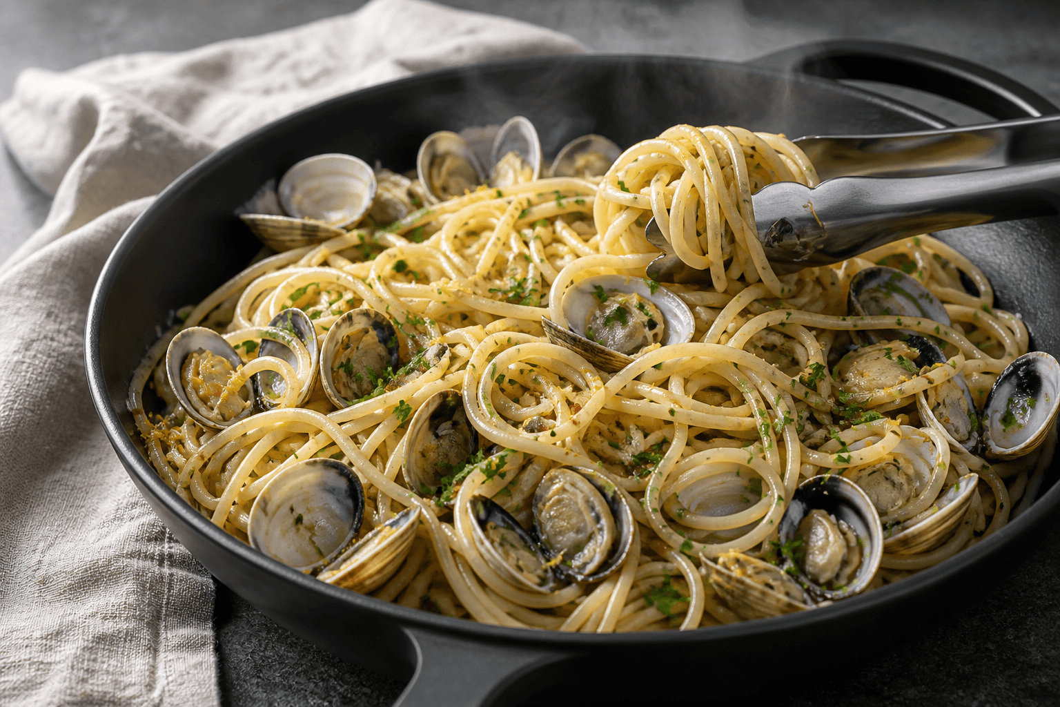 Blank spaghetti vongole med mange åbne muslinger, persille, chili og citron-gremolata i lav sort pande
