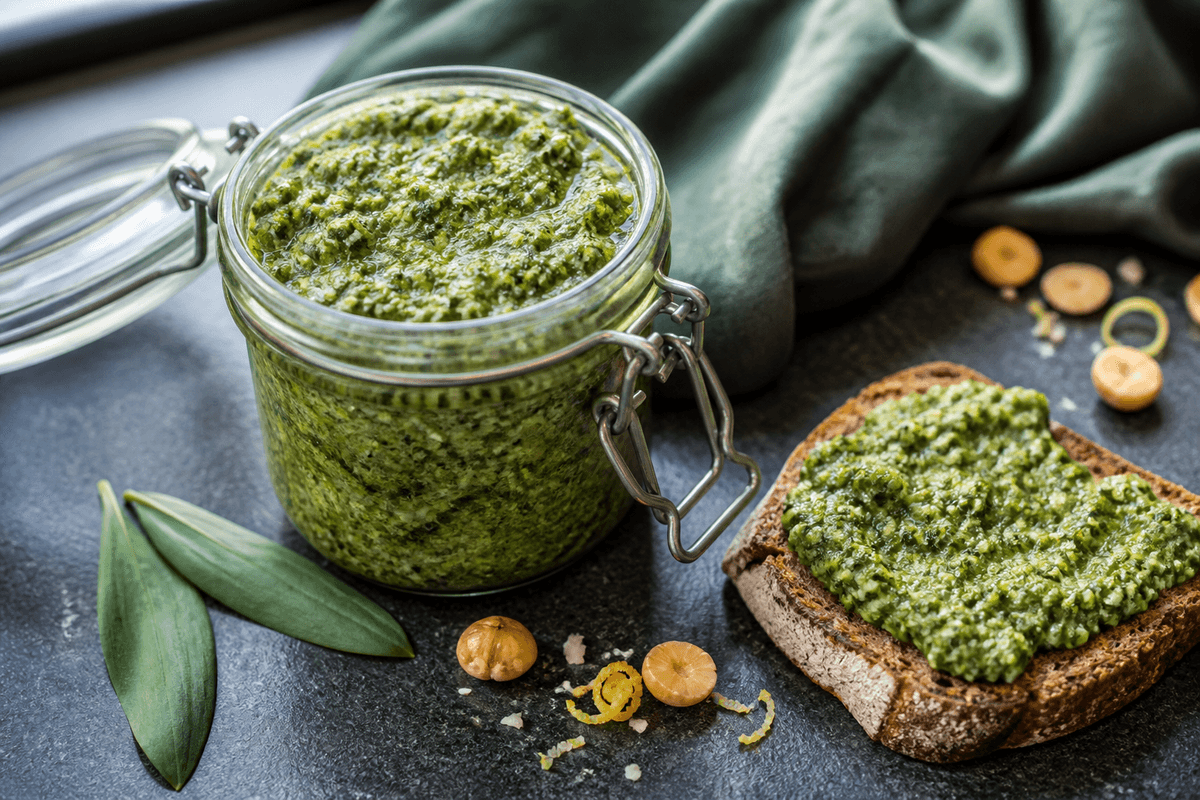 Klar grøn ramsløgspesto med hasselnød, lagret ost, citron og rapsolie i åbent patentglas ved ristet rugbrød