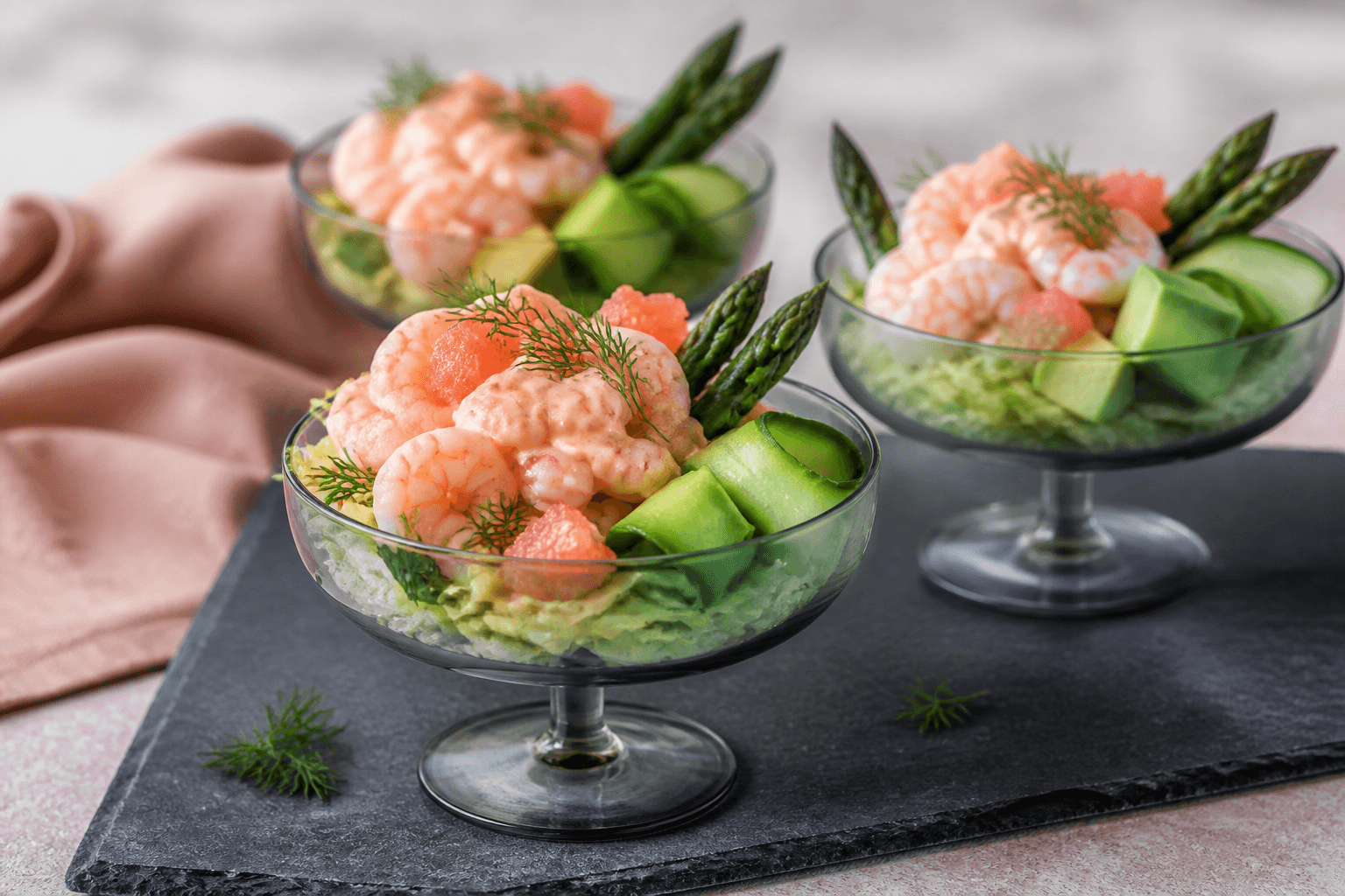 Tre moderne rejecocktails i røggrå coupes med kolde rejer, avocado, agurk, fennikel, asparges, grapefrugt og koralfarvet dressing