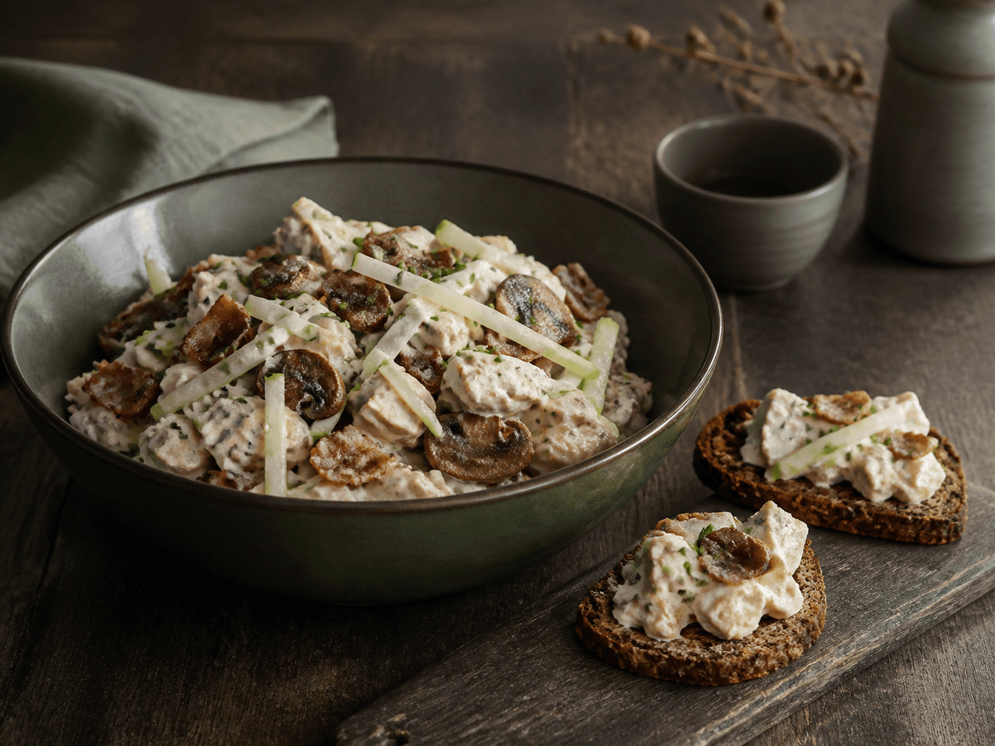 Rustik hønsesalat i mørkegrøn keramik med tydelige stykker kylling, sprød bacon, brunede svampe, syltet selleri, æble, sennepsskyr og purløg samt rugtoast