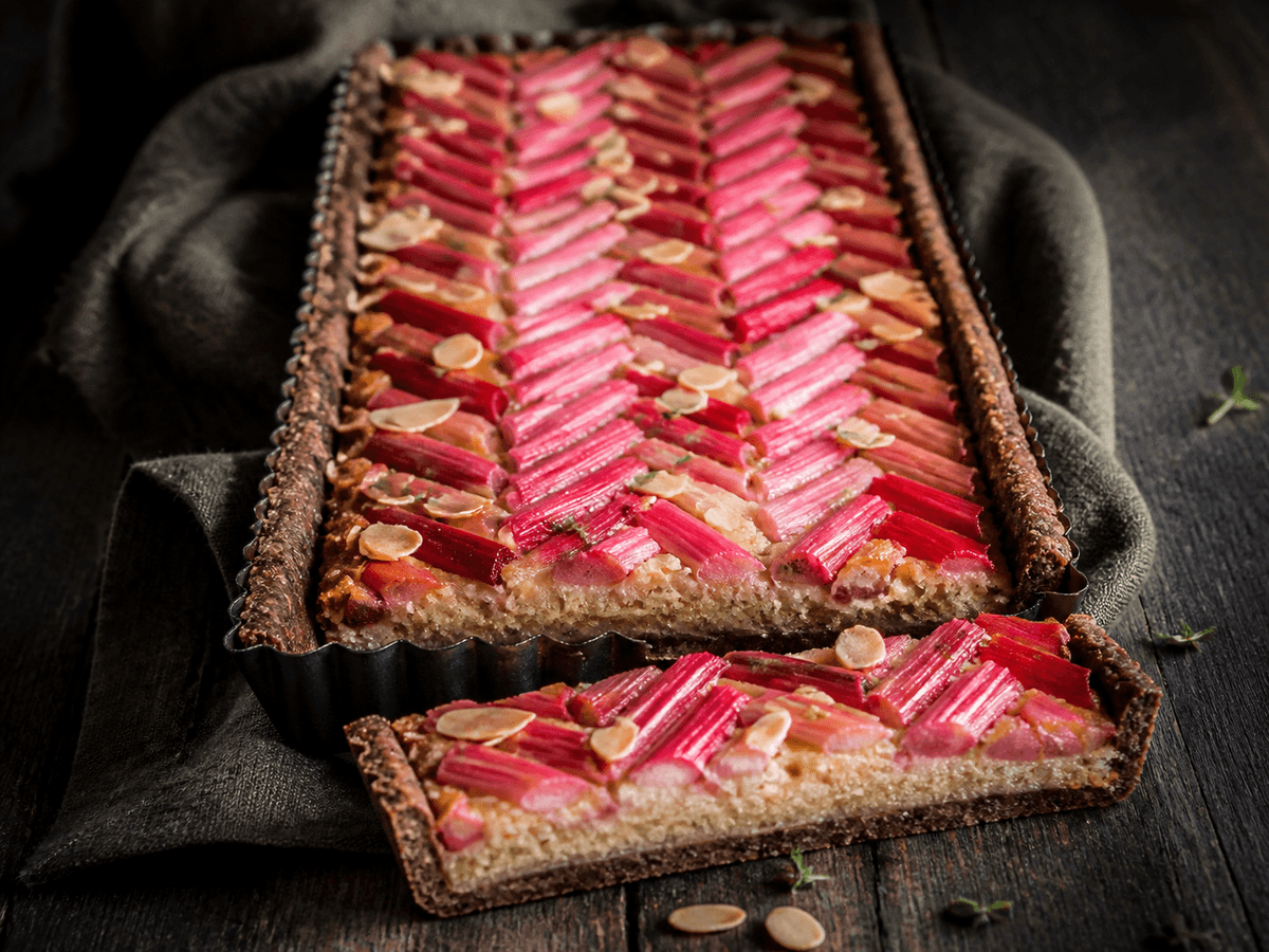 Rektangulær rabarbertærte med mørk rugmørdej, gylden mandelfrangipane, røde rabarber i sildebensmønster, mandelflager og citrontimian