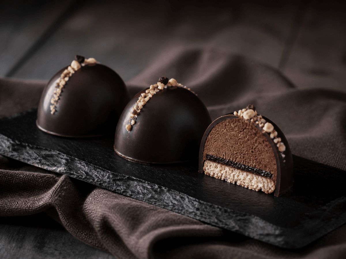 Tre lave mørke Sarah Bernhardt-kupler på sort skifer med hasselnød, espresso-rugmalttrøffel, tyndt solbærlag og blank tempereret chokoladeskal