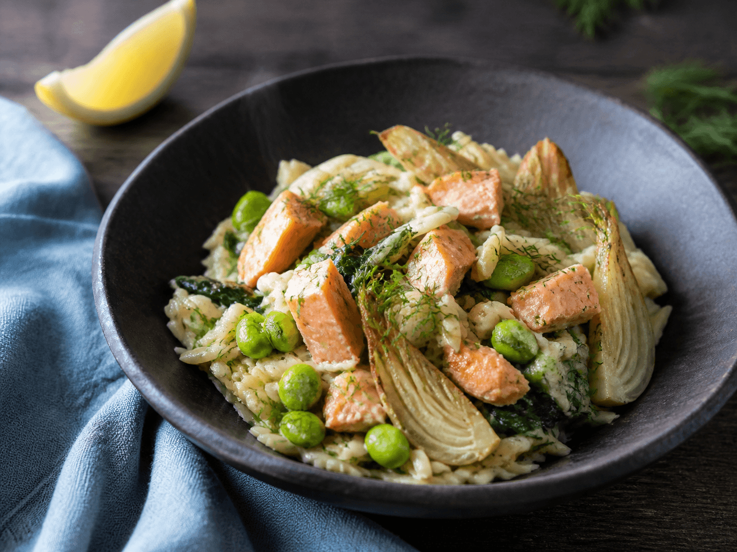 Cremet fuldkornsorzo i mat sort skål med varmrøget laks, edamame, bagt fennikel, spinat, citron og dild