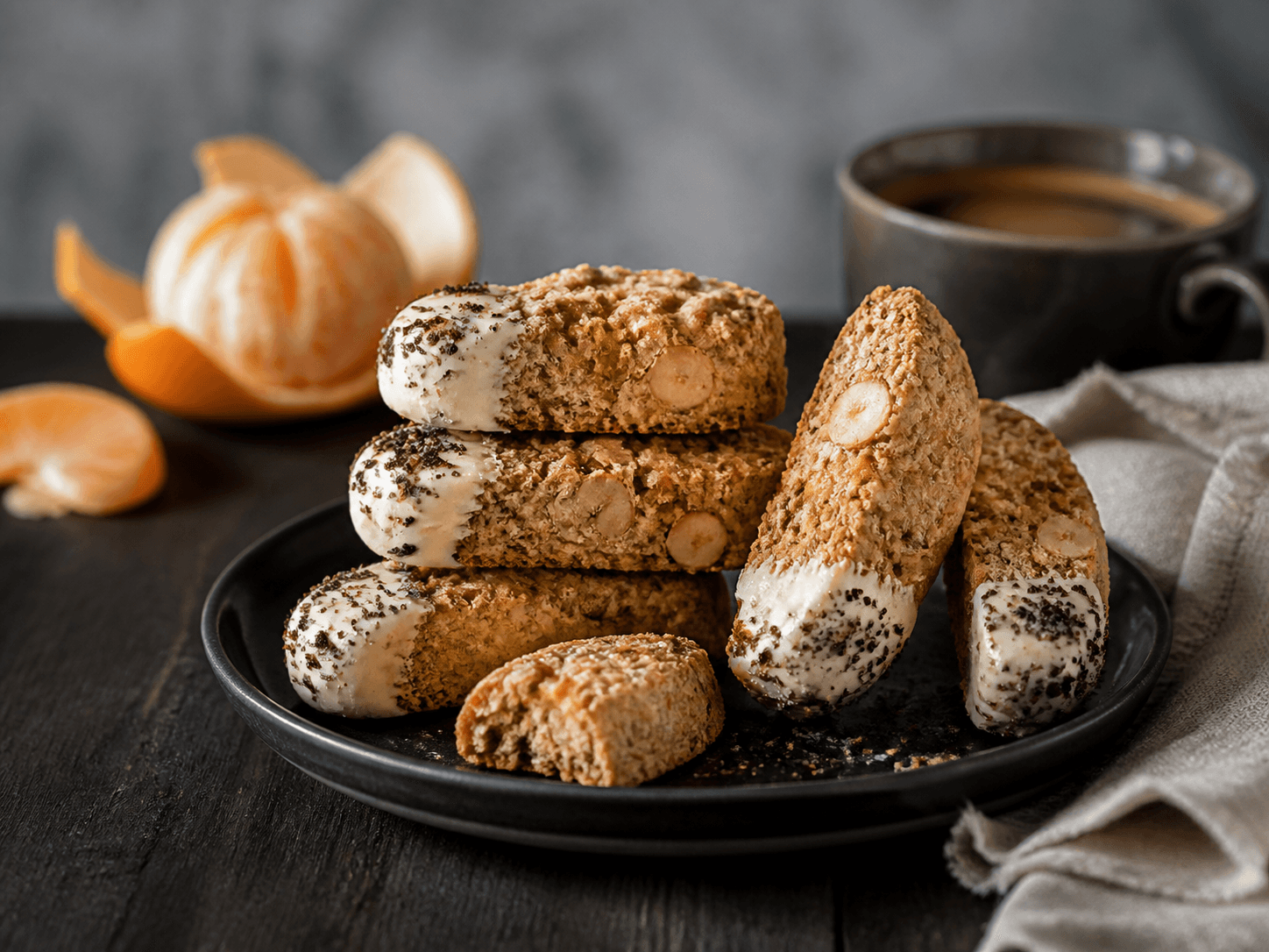 Korte mandarin-havrebiscotti med hasselnød, havtorn, hvid chokolade og maltdrys på sort tallerken