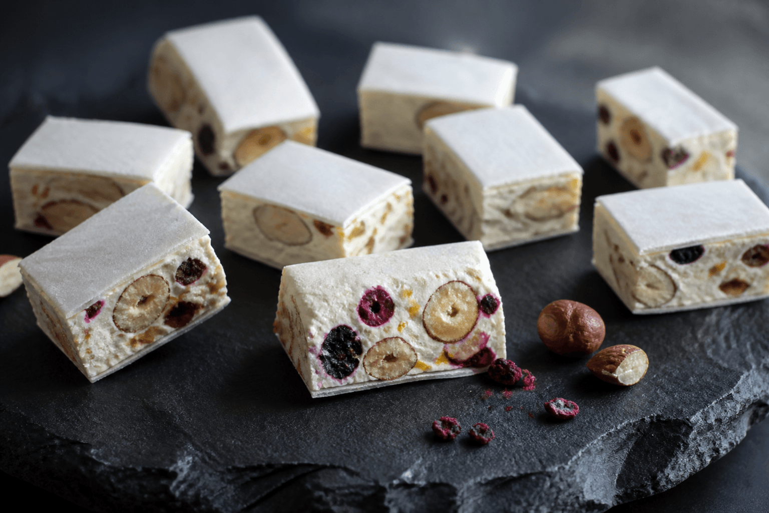 Tykke stykker fransk nougat med hasselnødder, mandler, solbær og appelsin mellem oblatpapir på mørk skifer