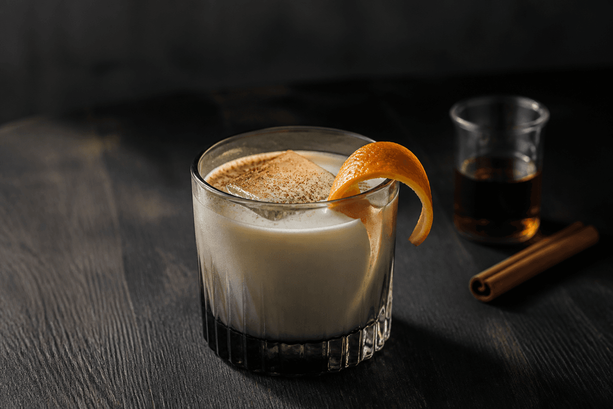 Cremet eggnog cocktail med mørk rom, appelsinskal, kardemomme og muskat over stor isterning i røget glas