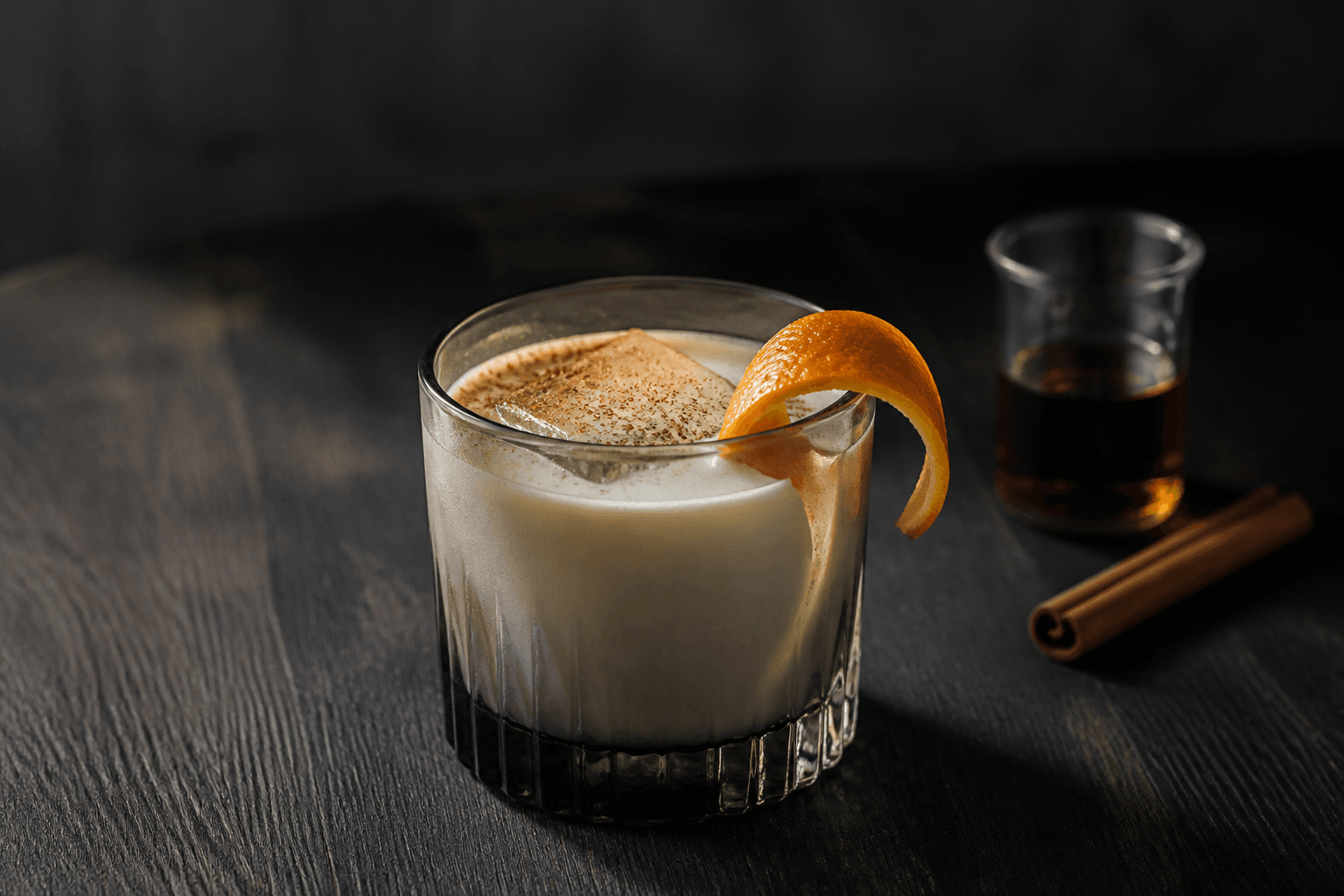 Cremet eggnog cocktail med mørk rom, appelsinskal, kardemomme og muskat over stor isterning i røget glas