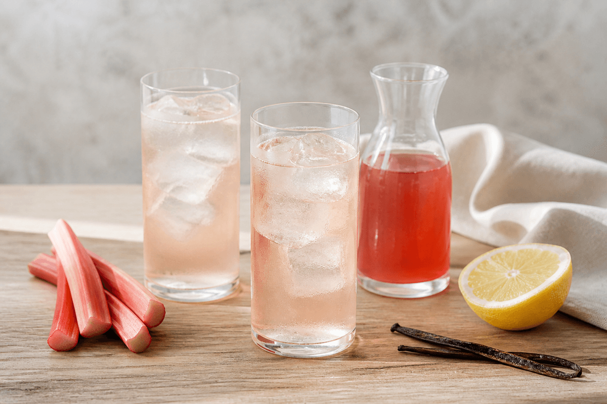 Lys rosa rabarbersaft med vanilje og citron i to iskolde glas og en lille kande koncentrat