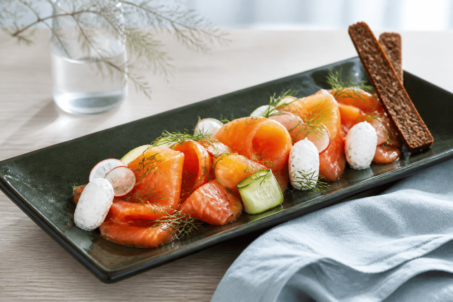 Tynde bånd af rubinorange gravad laks på langt mørkegrønt fad med peberrodsskyr, agurkebånd, radise, dild og smalle rugknæk