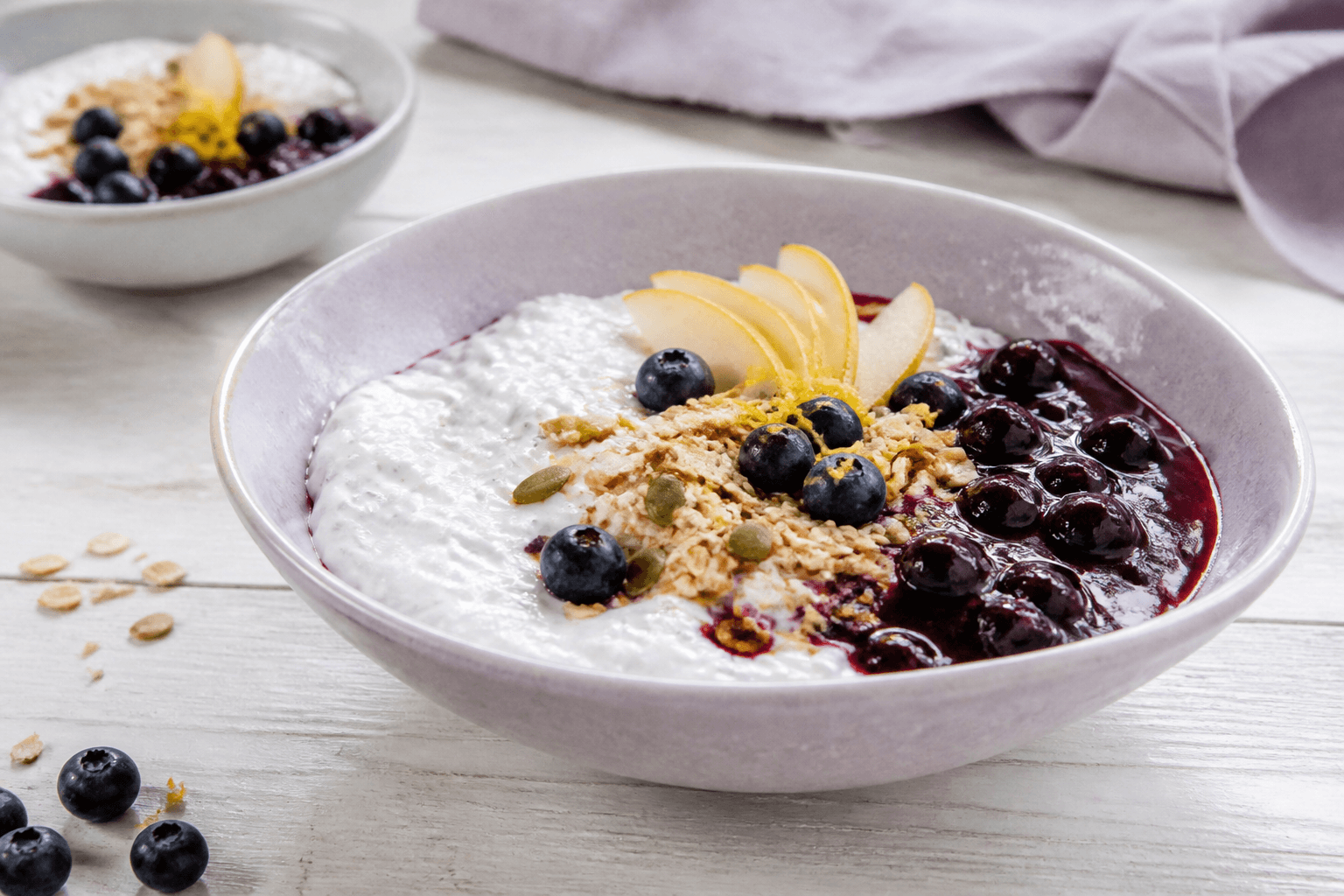 Lyslilla skål med cremet chiagrød og hytteost, blåbær-citronkompot, pære, friske bær og boghvedeknas
