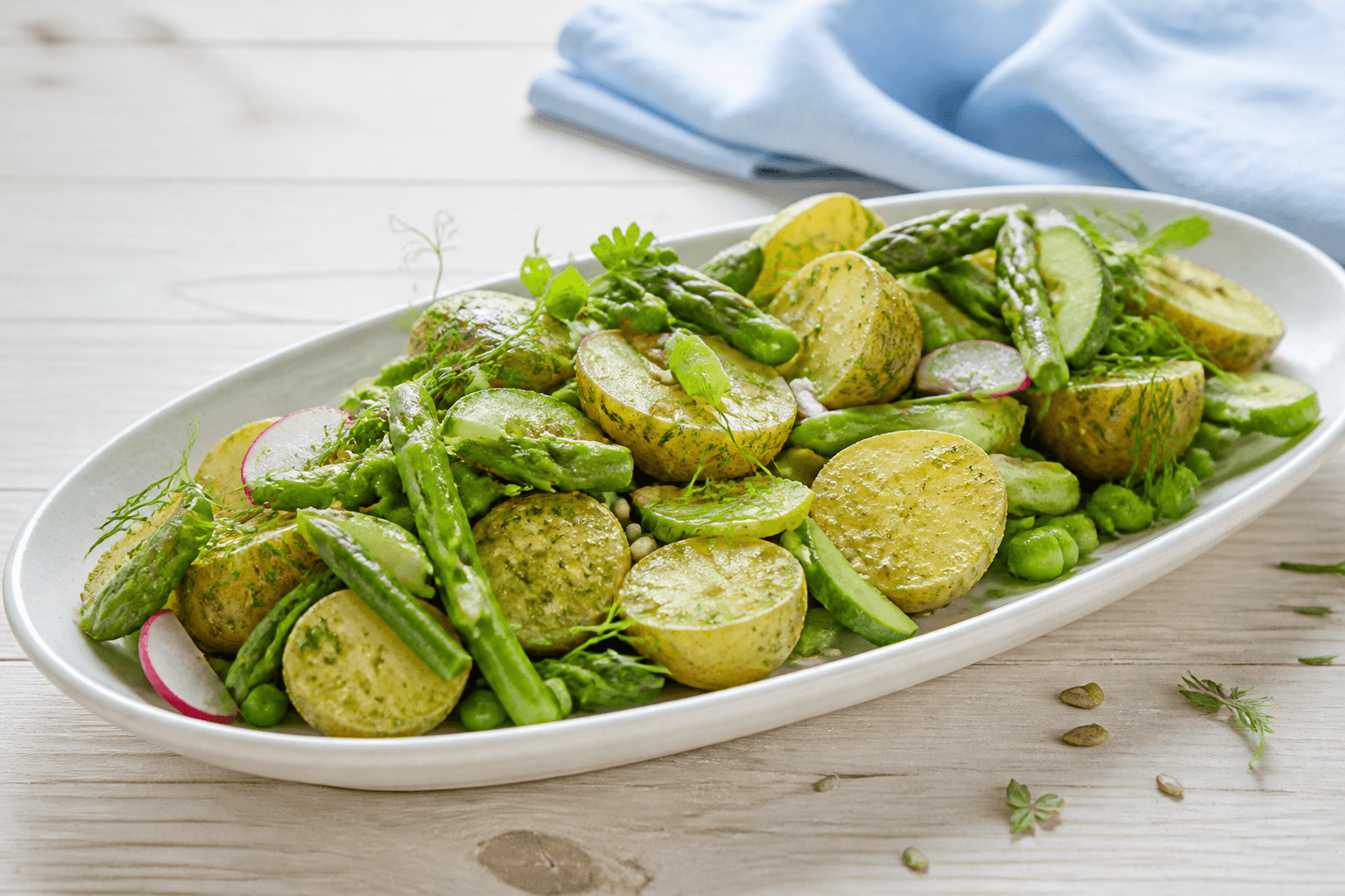 Green goddess kartoffelsalat med halve nye kartofler, asparges, ærter, radise og agurk på langt lyst fad