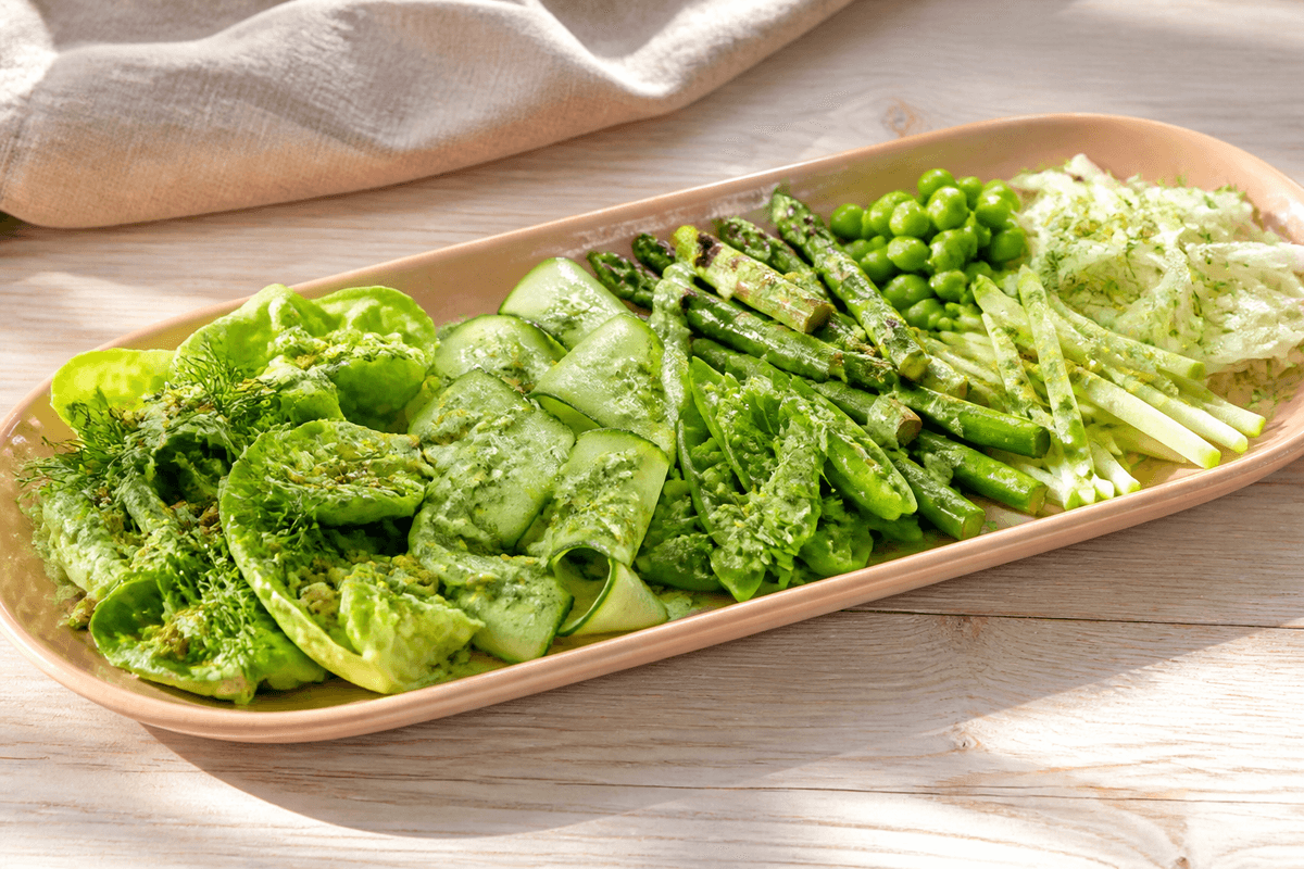 Komponeret green goddess-salat med hjertesalat, agurkebånd, grønne asparges, sukkerærter, grønne bønner, æble og urtedressing på koralfad