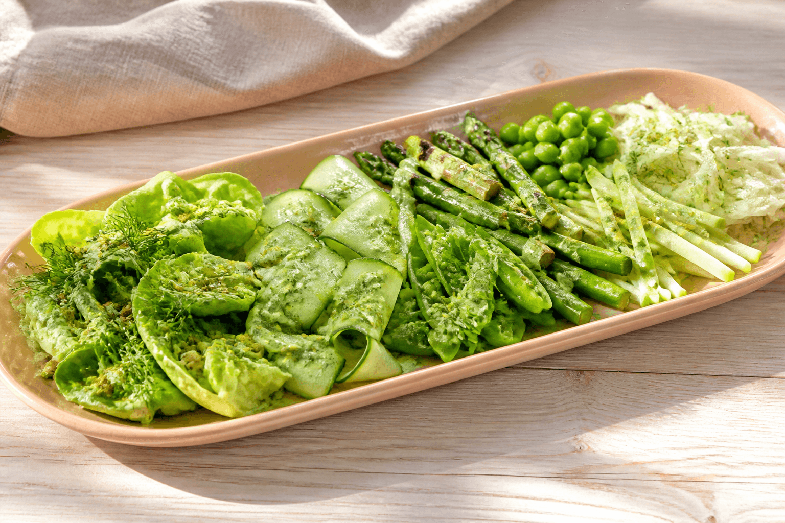 Komponeret green goddess-salat med hjertesalat, agurkebånd, grønne asparges, sukkerærter, grønne bønner, æble og urtedressing på koralfad