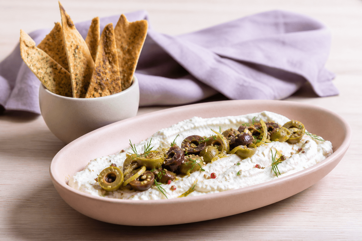Silkeblød rørt feta i rosa langskål med grønne og Kalamataoliven, citron, dild og sprøde zaatar-pitachips i separat kop