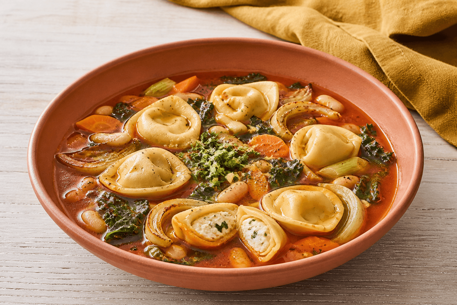 Terrakottaskål med rød tomat-fennikelbouillon, tortellini, hvide bønner, grønkål, gulerod og én åben varm ricottafyldning