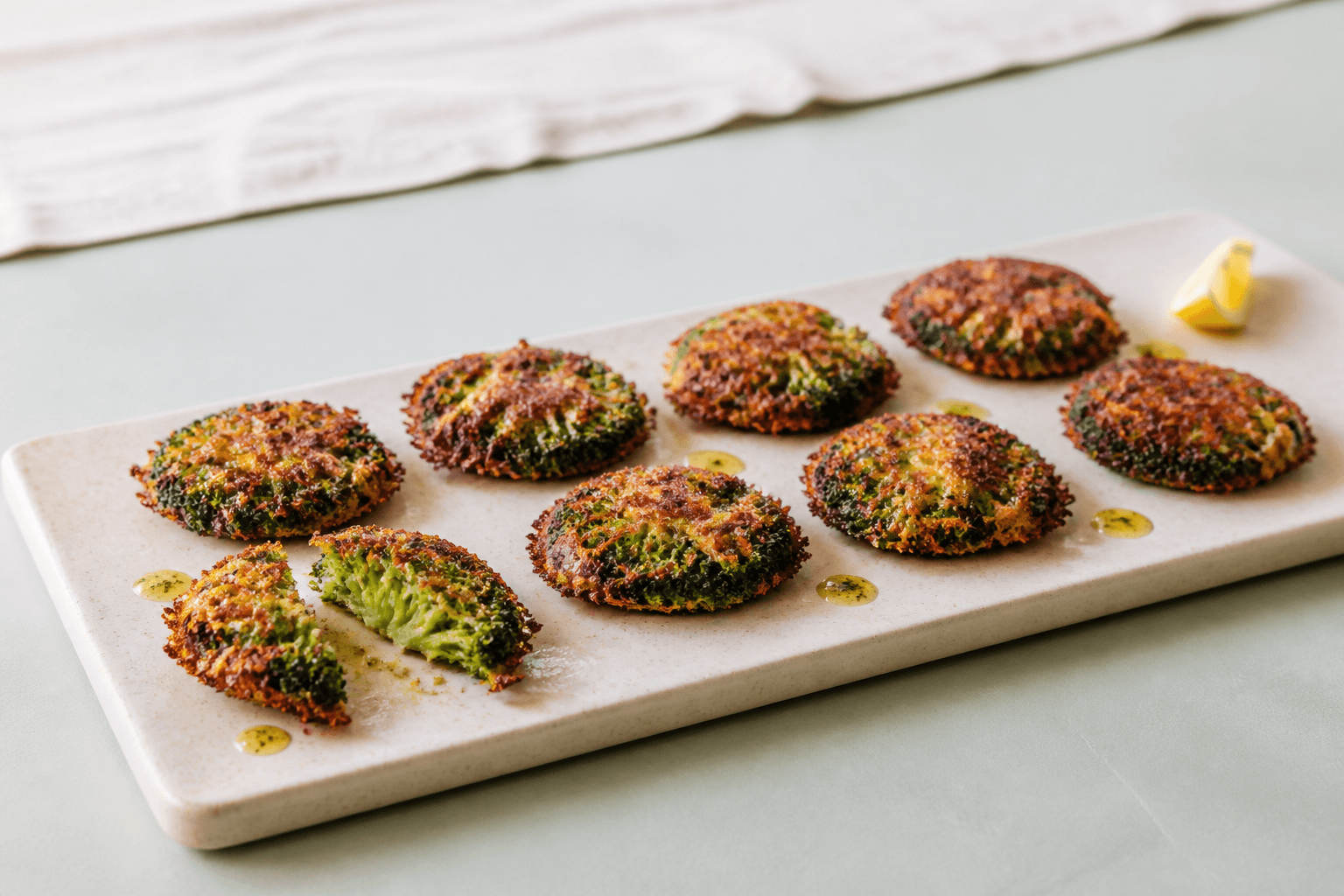 Otte knuste broccoli-rosetter i to rækker på sandfarvet fad med sprød cheddarhalo, røget paprika, citronolie og ét åbent stykke