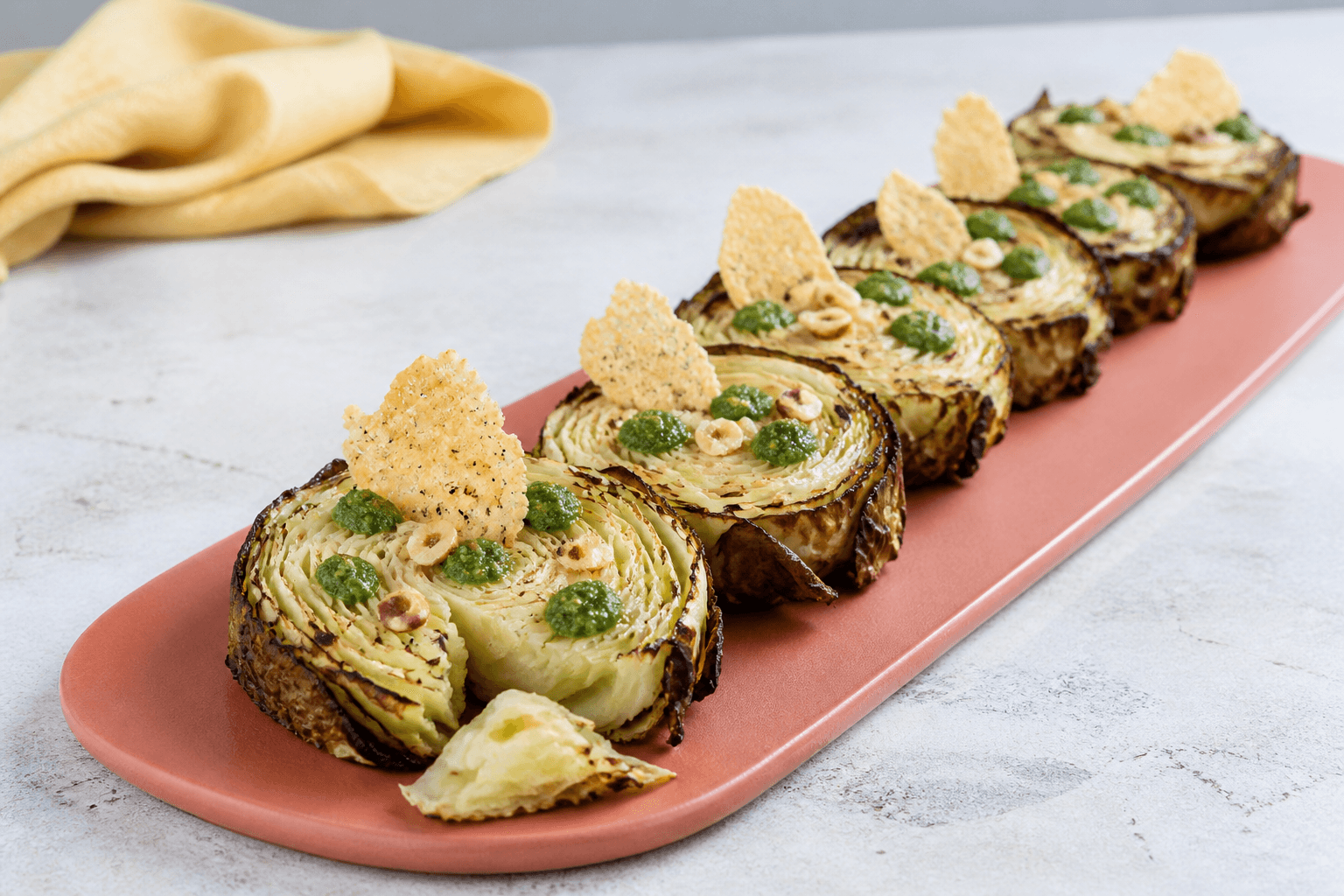 Seks ristede spidskålsrosetter på koralfad med grøn basilikum-hasselnøddepesto, sprøde parmesansejl og ristede nødder