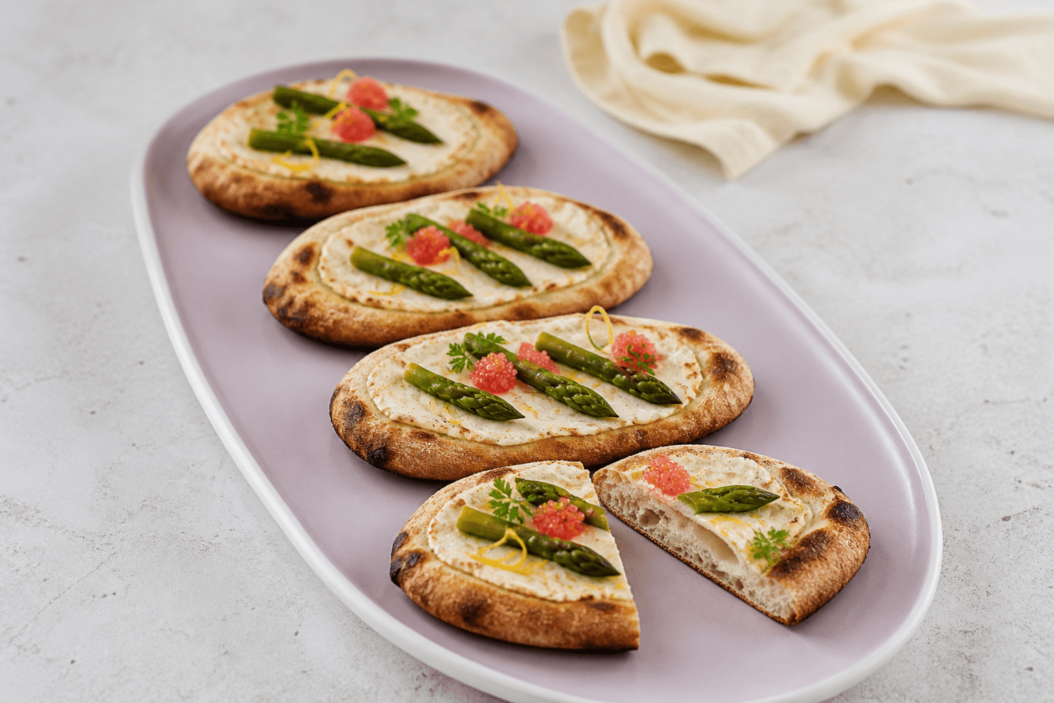 Tre hele ovale pizzette og én åbnet pizzetta på støvet lilla fad med sprød luftig kant, mascarpone, grønne asparges og kold rød stenbiderrogn