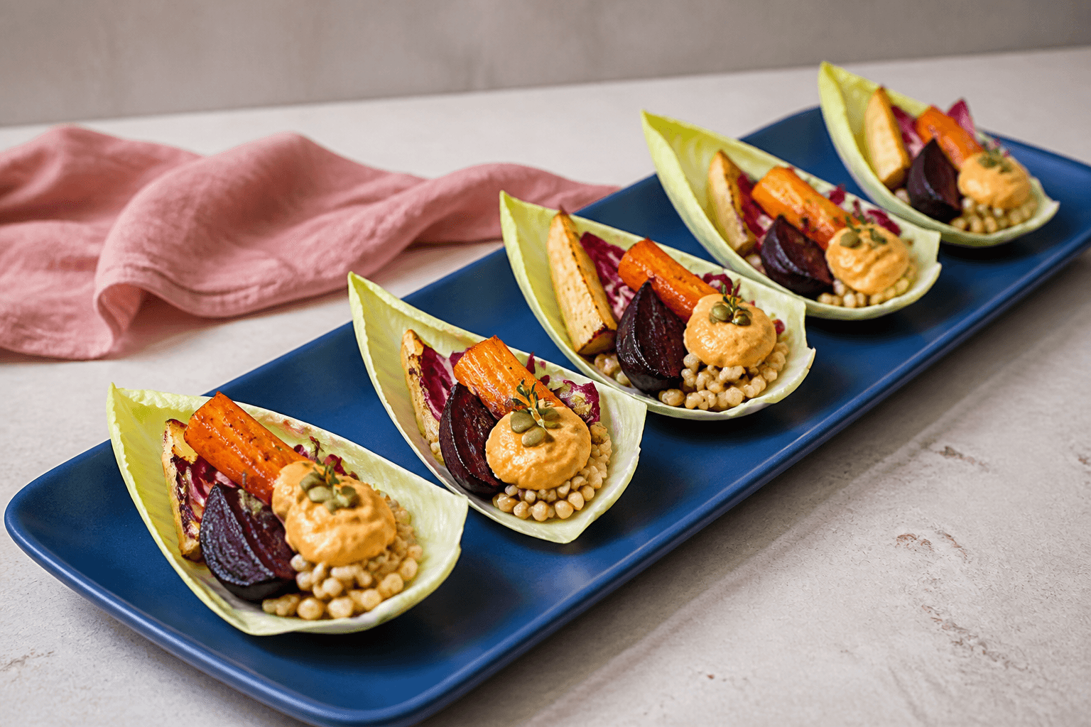 Fem spidskålsbåde på koboltblåt fad med bagte rødbeder, gulerødder, pastinak, perlebyg, radicchio, orange-tahinidressing, græskarkerner og timian