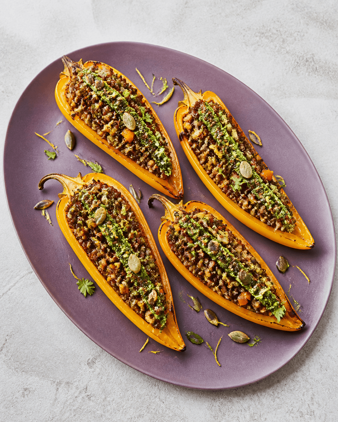 Fire åbne gule peberfrugthalve på auberginefarvet fad med rød quinoa, grønne linser, svampe, gulerod og persillekernepesto