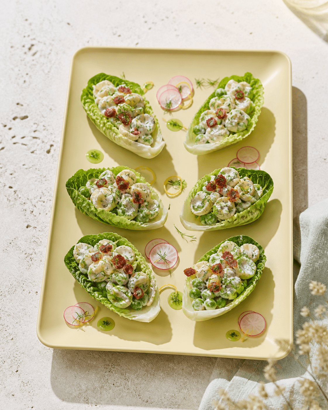 Seks sprøde salatbåde på smørgult fad fyldt med orecchiette, ærter, kold dilddressing, bacon, radise og citron