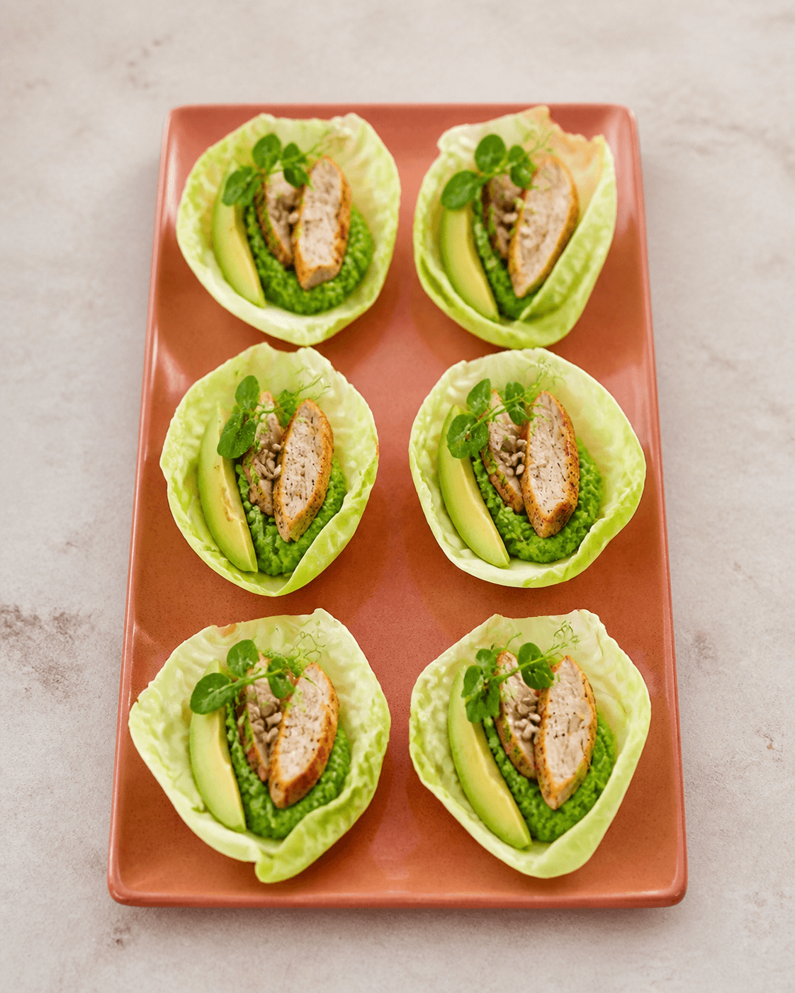 Seks spidskålsparceller på terrakottafad med gennemstegt kylling, ærte-urtecreme, avocado, solsikkekerner og ærteskud