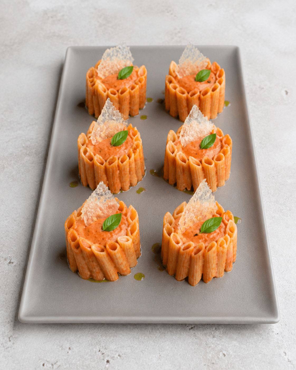 Seks opretstående penne-timbaler på varmgråt fad med koral tomatflødesauce, parmesansejl, basilikum og urteolie