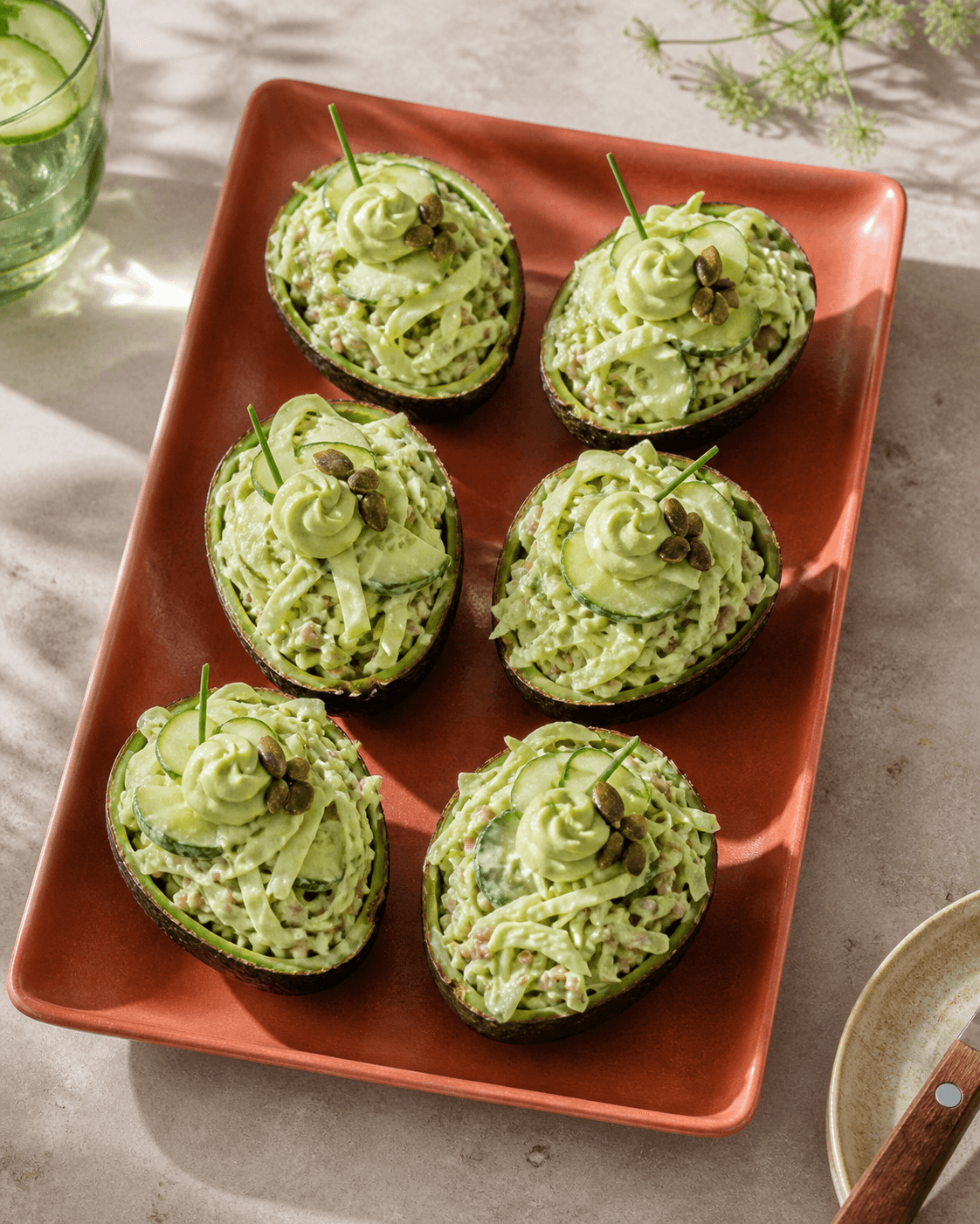 Seks avocadoskaller på brændt orange fad fyldt med cremet spidskål, agurk, hvedekerner, avocadocreme, purløg og græskarkerner