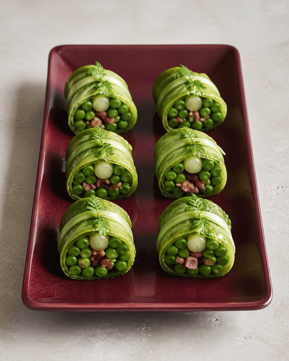 Seks braiserede salatroulader på bordeauxfad med ærter, sprød bacon, perleløg, porrebånd og kørvel