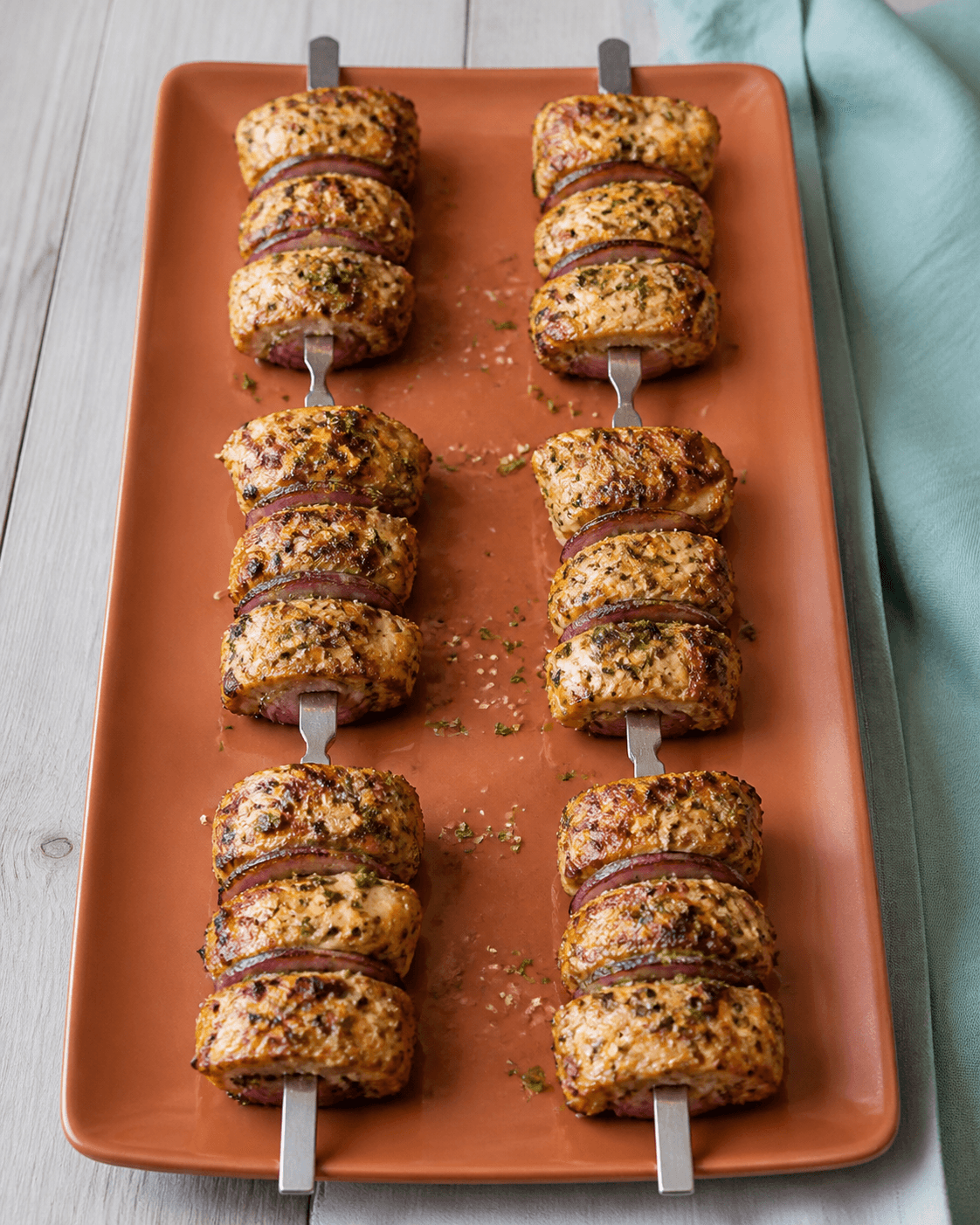 Seks metalspyd med gylden gennemstegt kylling, rødløg, grøn urteolie, sesam og persille på terracottafad