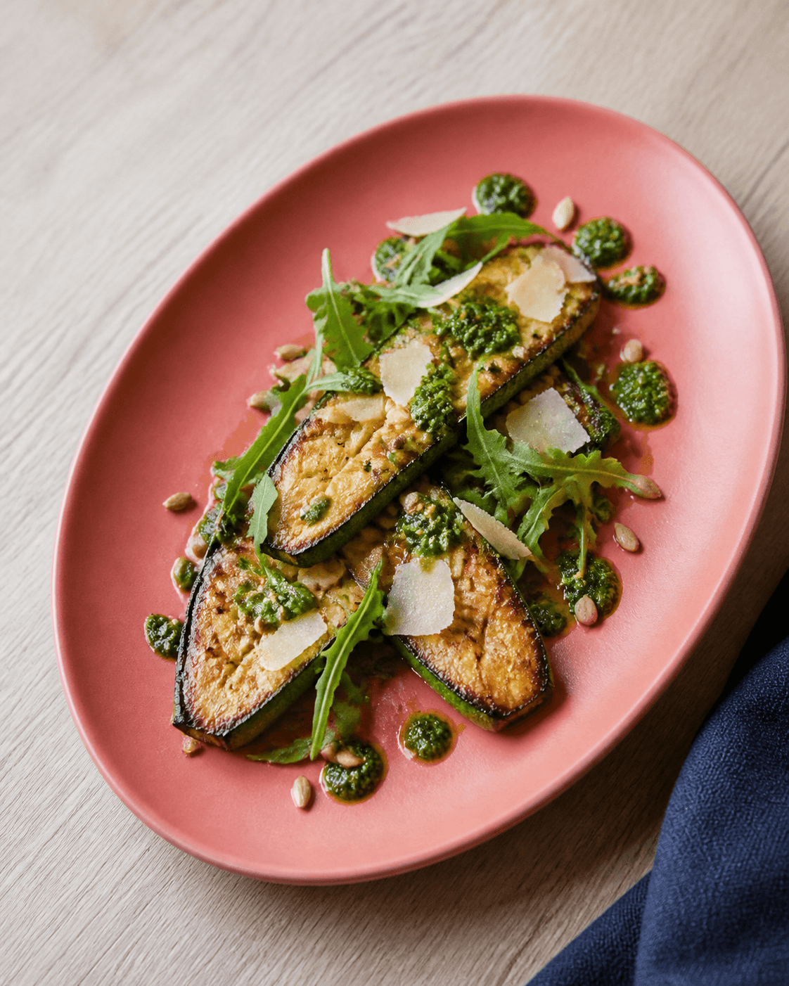 Tre gyldent stegte squashplanker med krydsridser, rucola, basilikum-mandelpesto, parmesanflager og solsikkekerner på koralfarvet fad