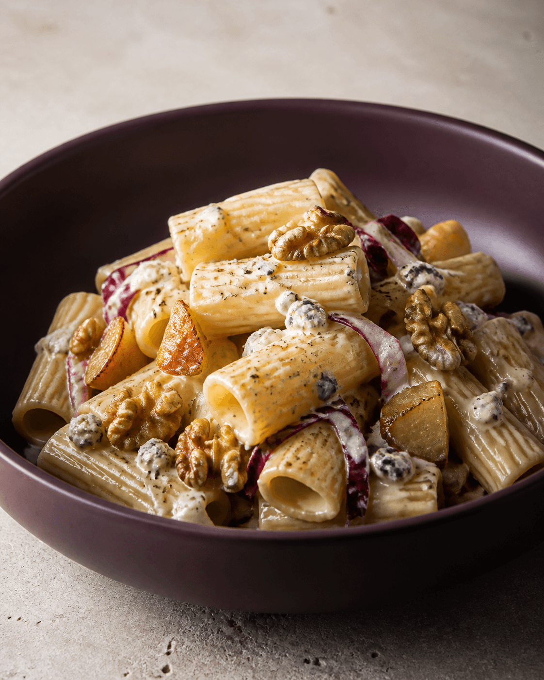 Rigatoni i cremet gorgonzolasauce med ristede pæretern, valnødder, radicchio og sort peber i dyb auberginefarvet skål